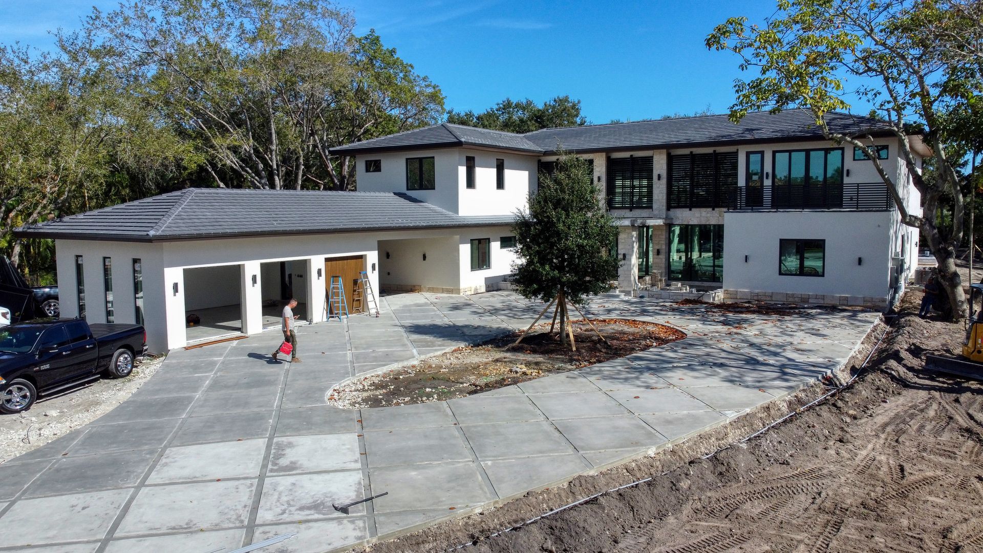 Modern white two-story house with a detached garage. Concrete driveway, small tree, and a person walking in front.
