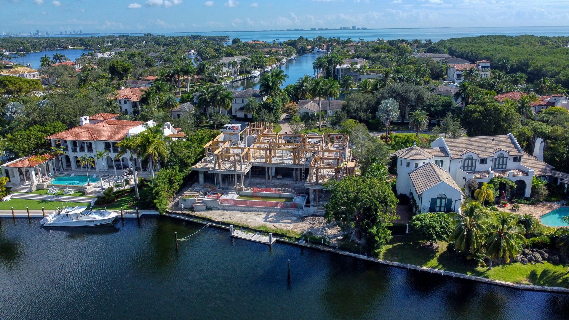 Waterfront houses with a house under construction. Trees, water, and blue sky.