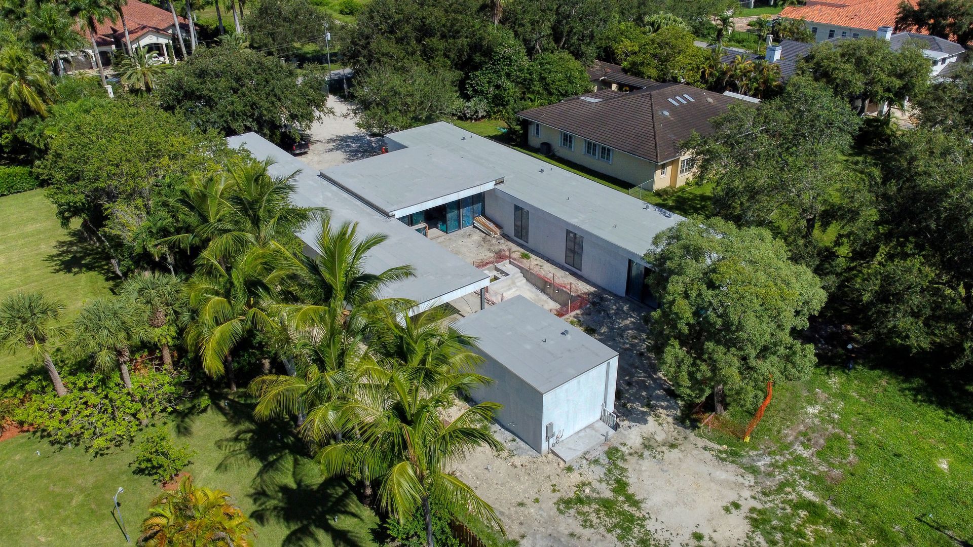 Aerial view of a modern, flat-roofed house surrounded by greenery. Gray siding, visible driveway.
