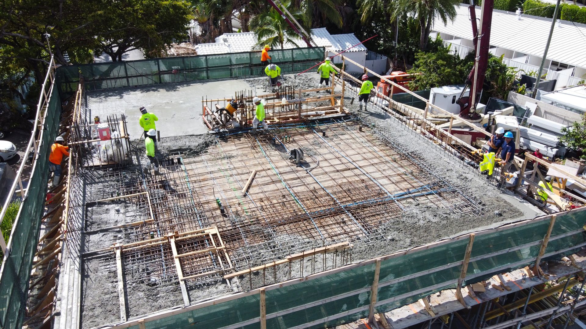 Construction workers pouring concrete at a work site. Green safety netting surrounds the area.