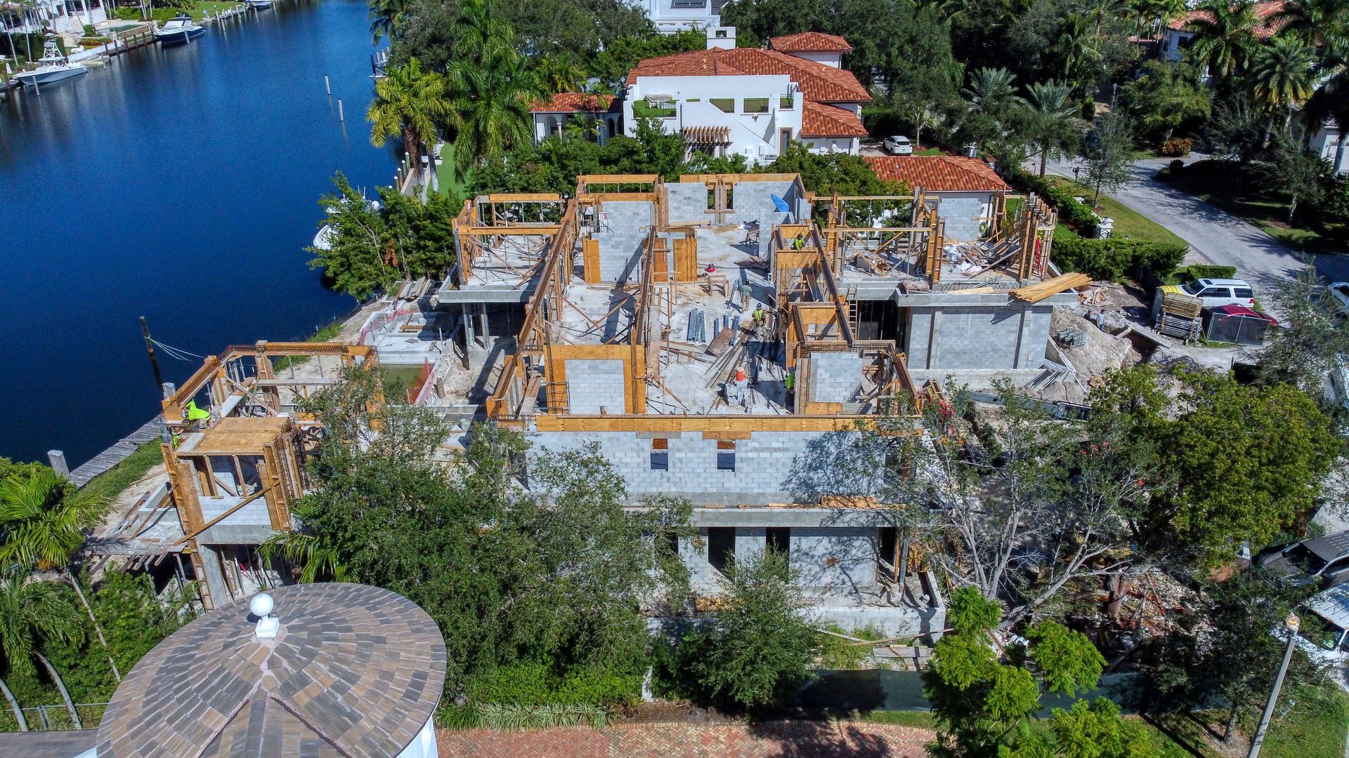Aerial view of a home under construction; partially demolished roof, surrounded by water and trees.