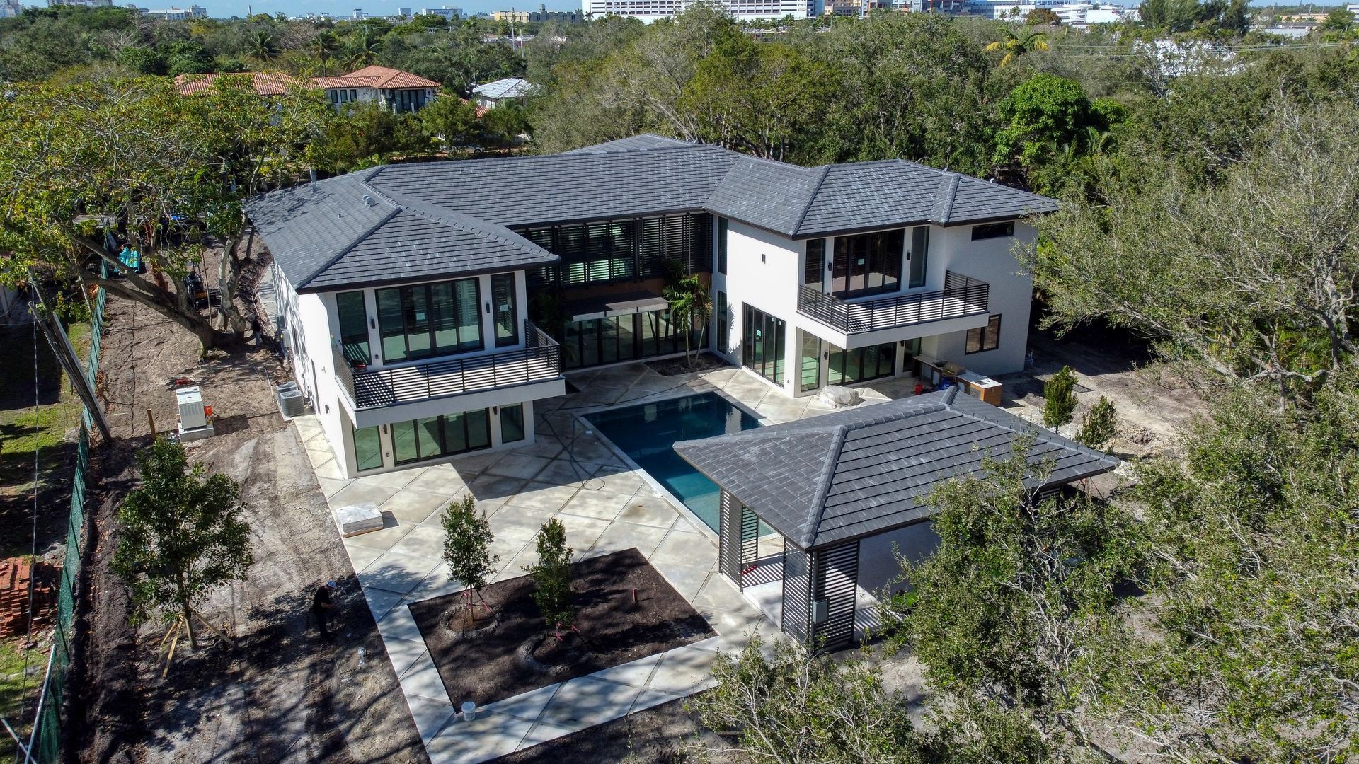 Modern white house with dark roof, pool, and surrounding trees.