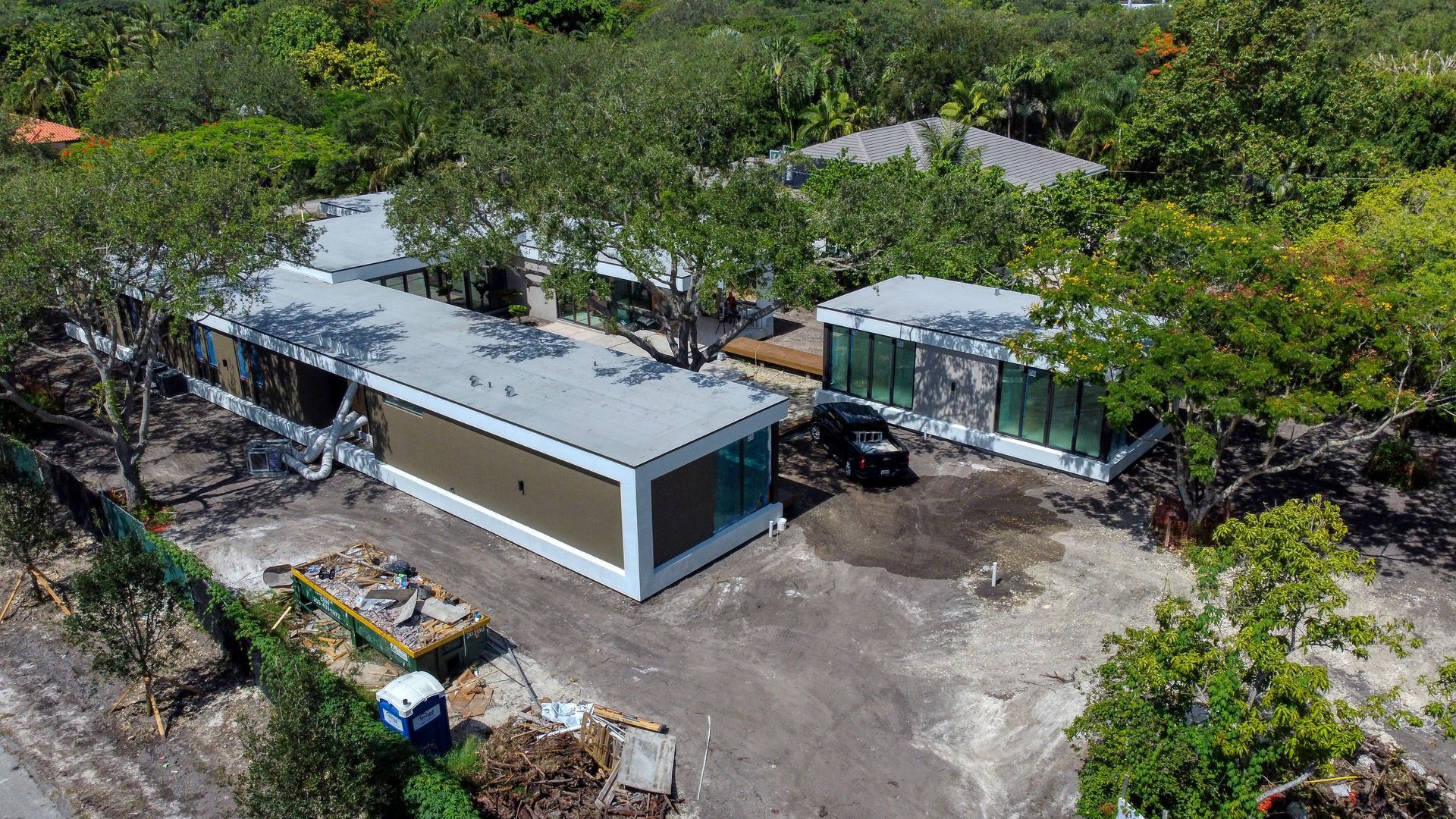 Modern homes under construction, surrounded by trees. Dark, rectangular buildings with white trim.