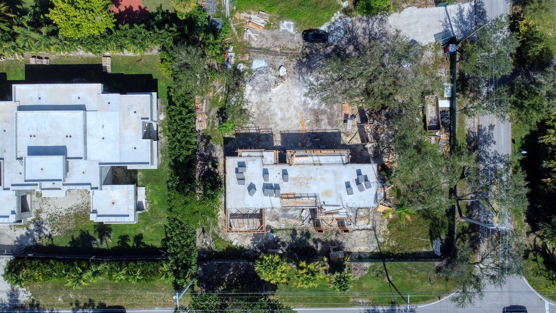 Aerial view of construction site with partial foundation, surrounded by trees and a road.