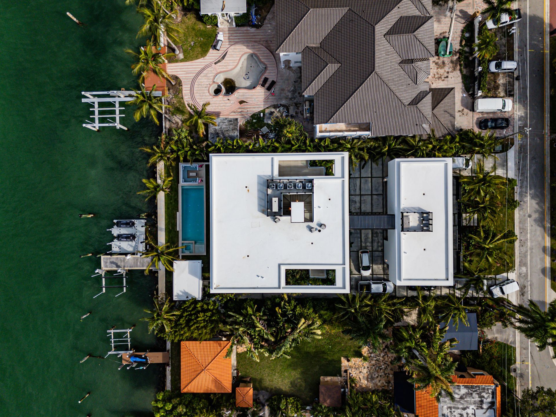 Aerial view of waterfront houses with docks, pool, and green vegetation in a tropical setting.