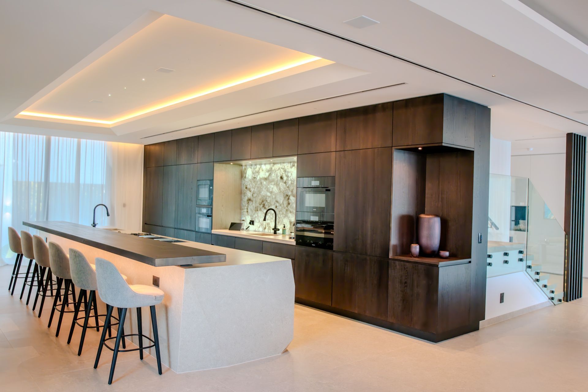 Modern kitchen with dark wood cabinets, large island with bar stools, and marble backsplash.