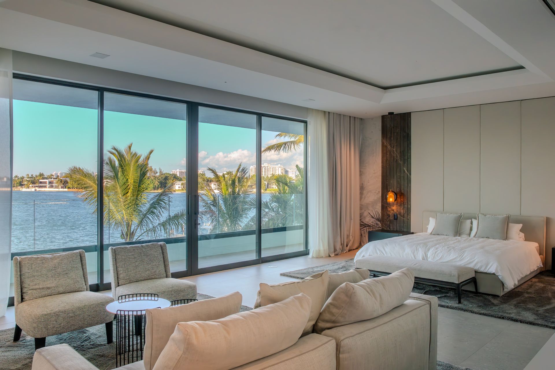 Bedroom with large windows, lake view, neutral colors, modern furniture, and a bed.