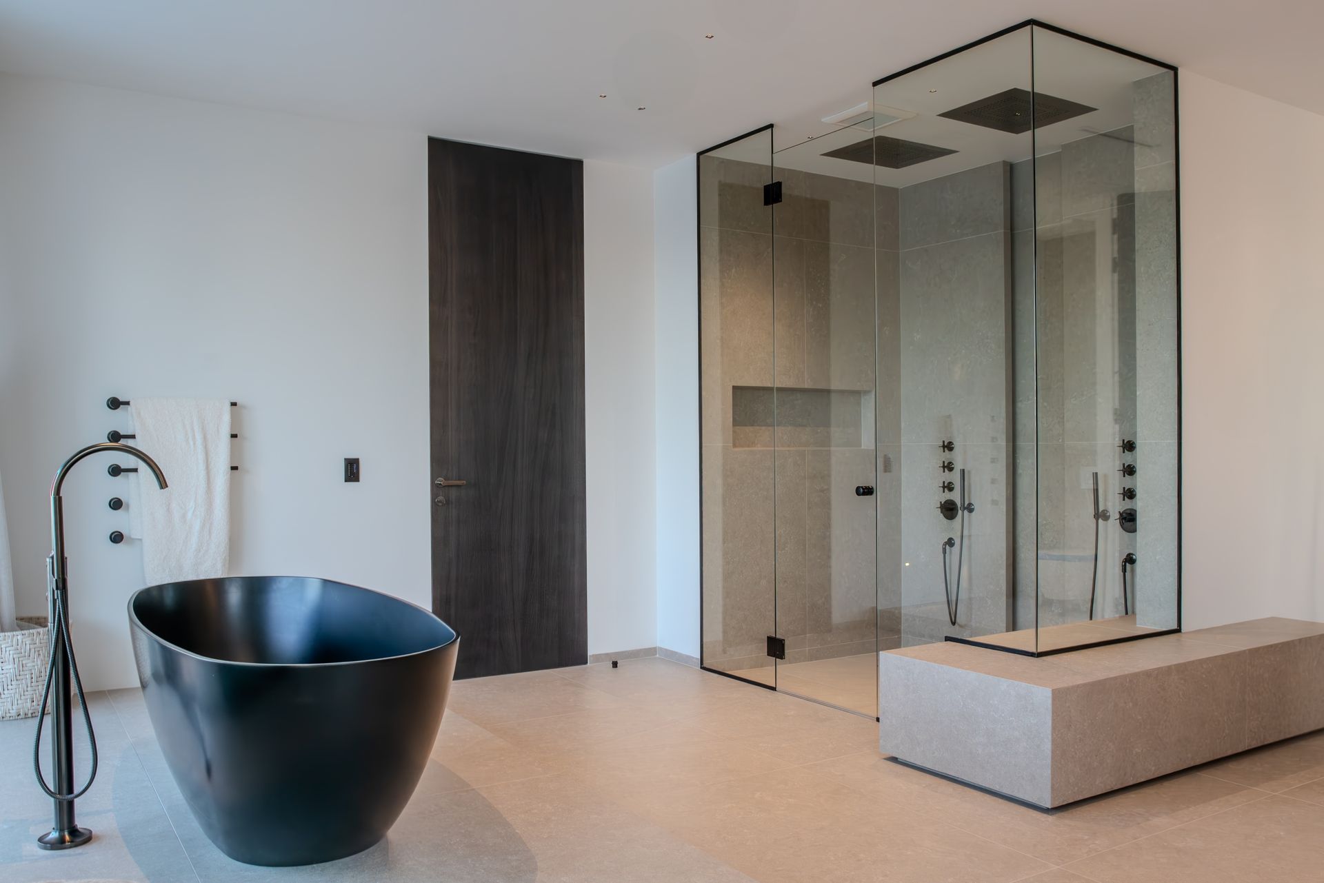 Modern bathroom with a black tub, glass shower, and light stone bench.