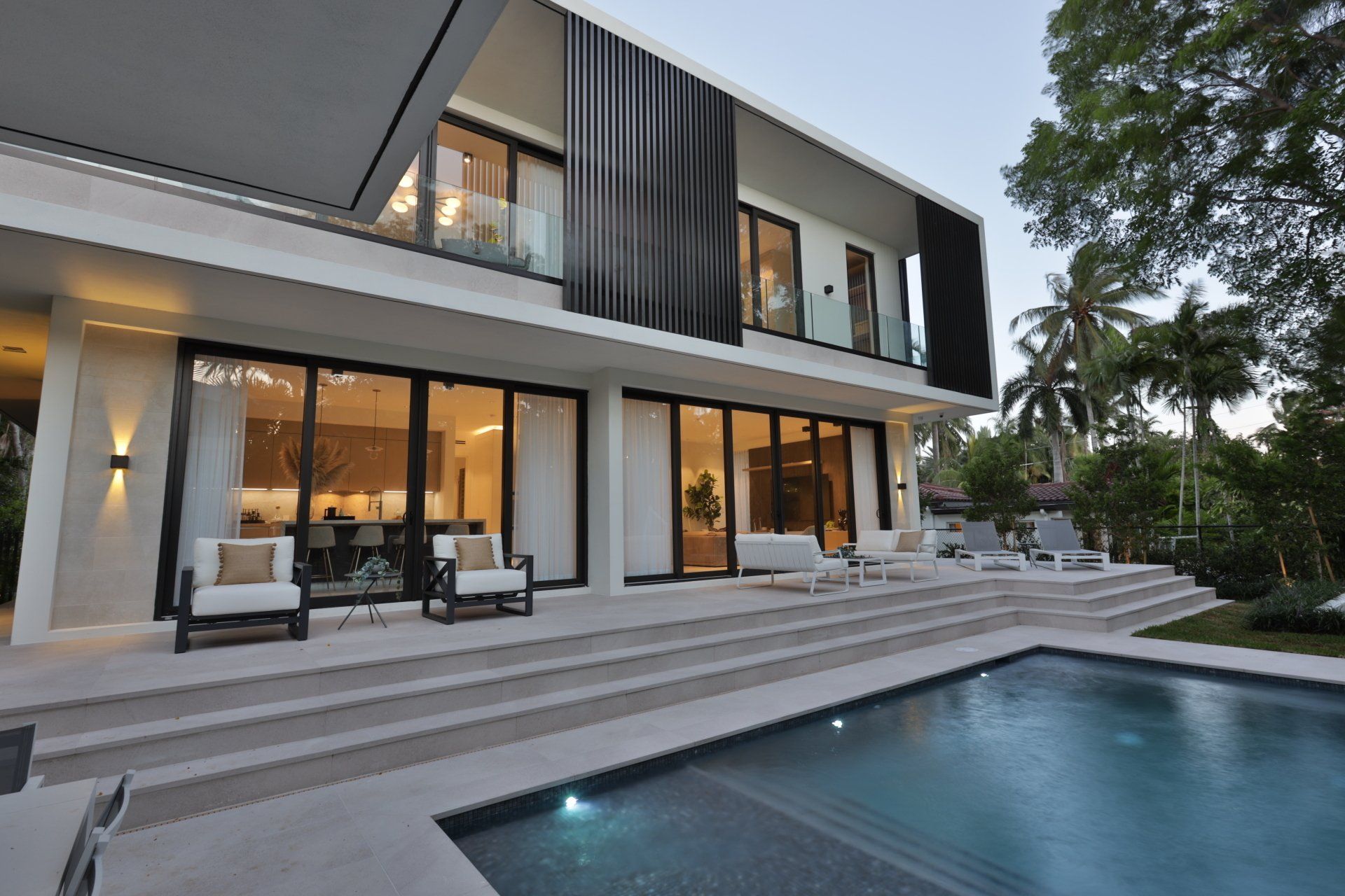 Modern house with a pool and patio. White and dark accents. Palm trees in the background.