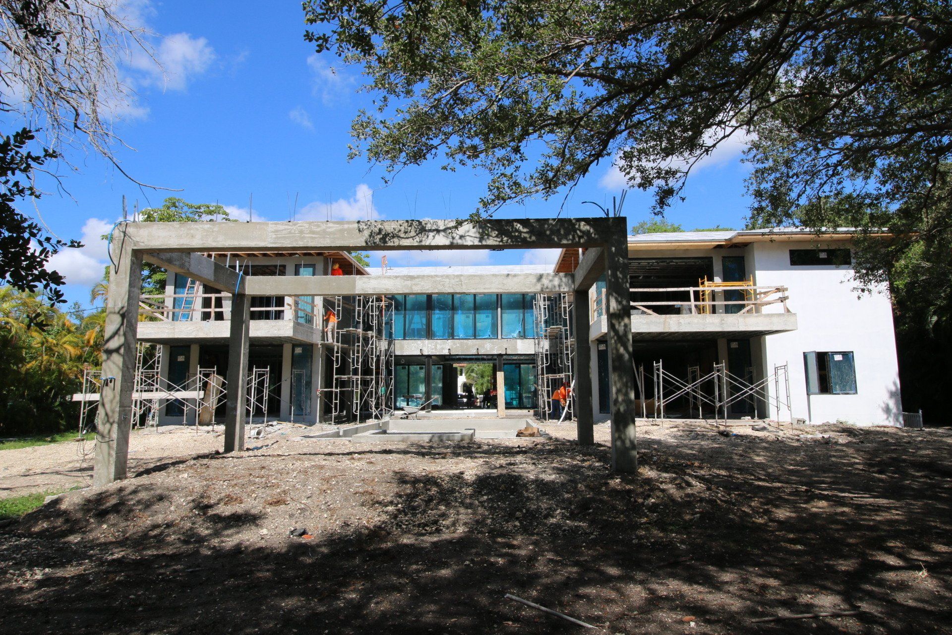 A modern house under construction with concrete beams and glass walls. Outdoors, sunny.