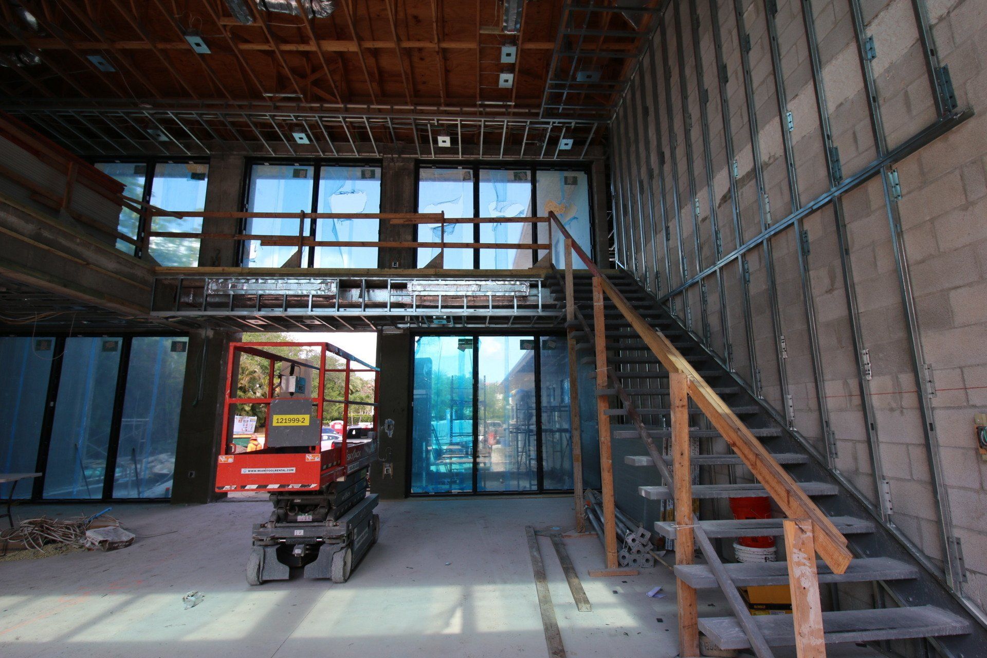 Interior of a building under construction, featuring unfinished walls, stairs, windows, and a lift.