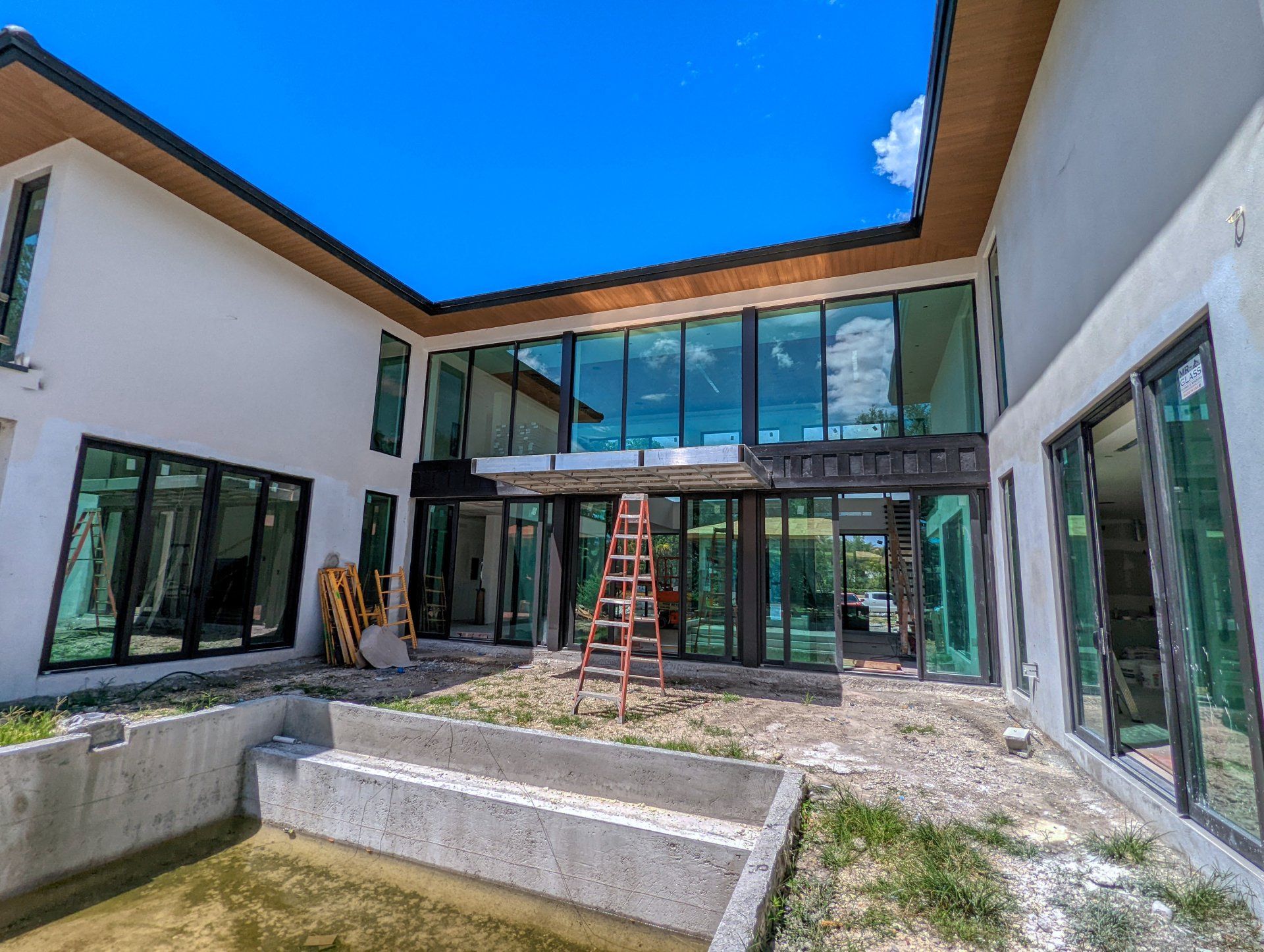 Modern house exterior with large windows under construction; ladder visible.