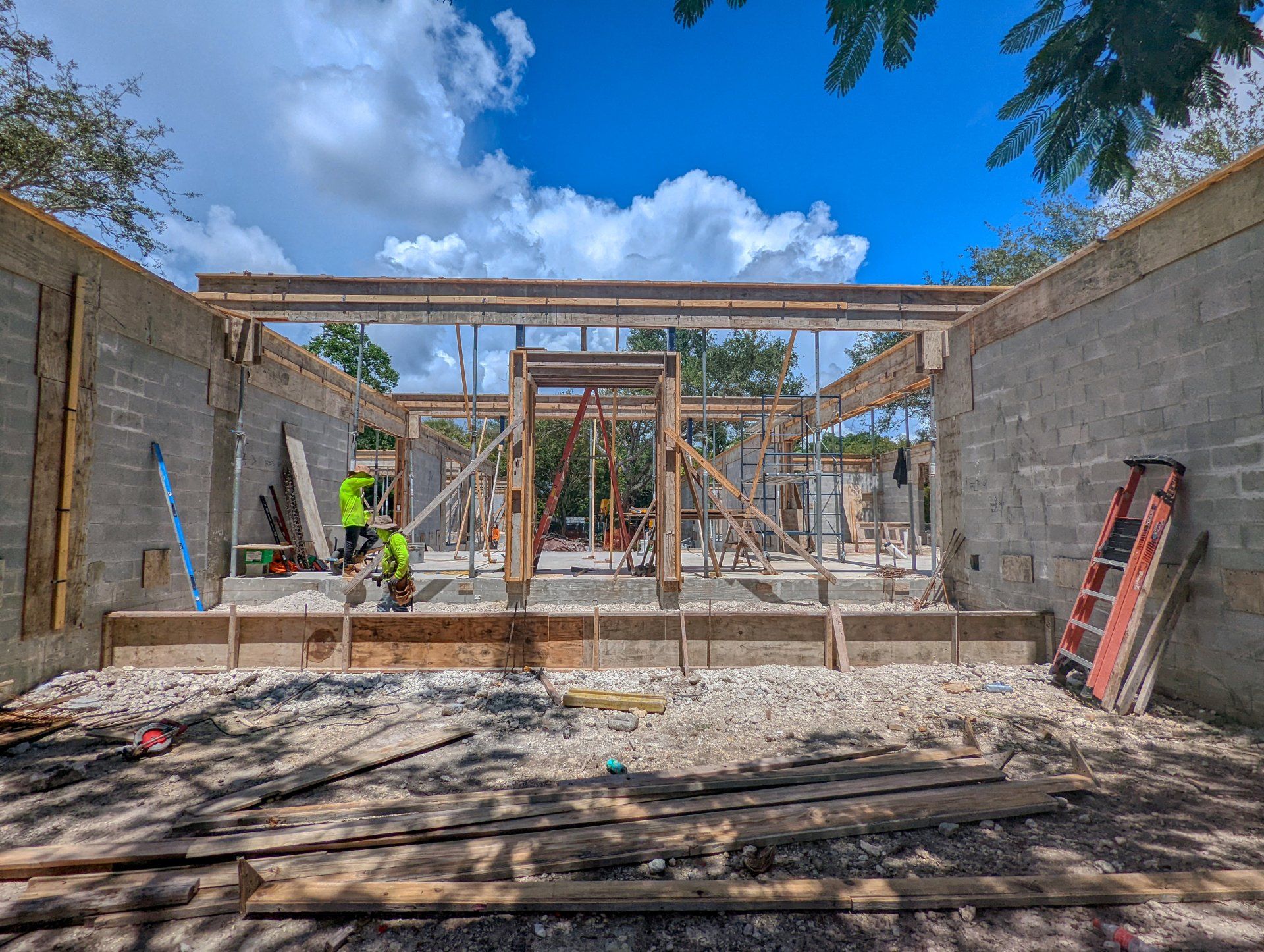 Construction site: Concrete walls with wooden framing and a worker in neon vest under a blue sky.