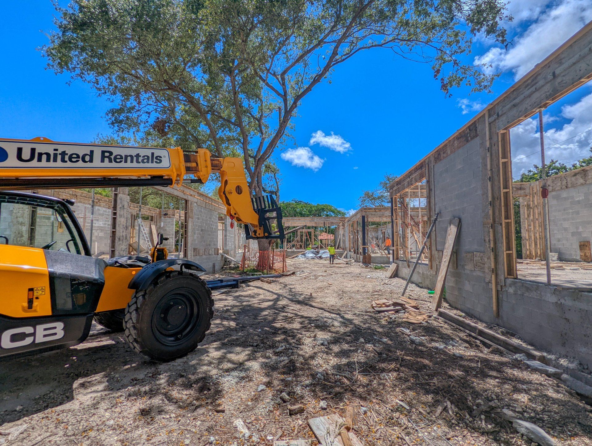 Construction site with a yellow JCB telehandler; partially built concrete and wood structures under a blue sky.