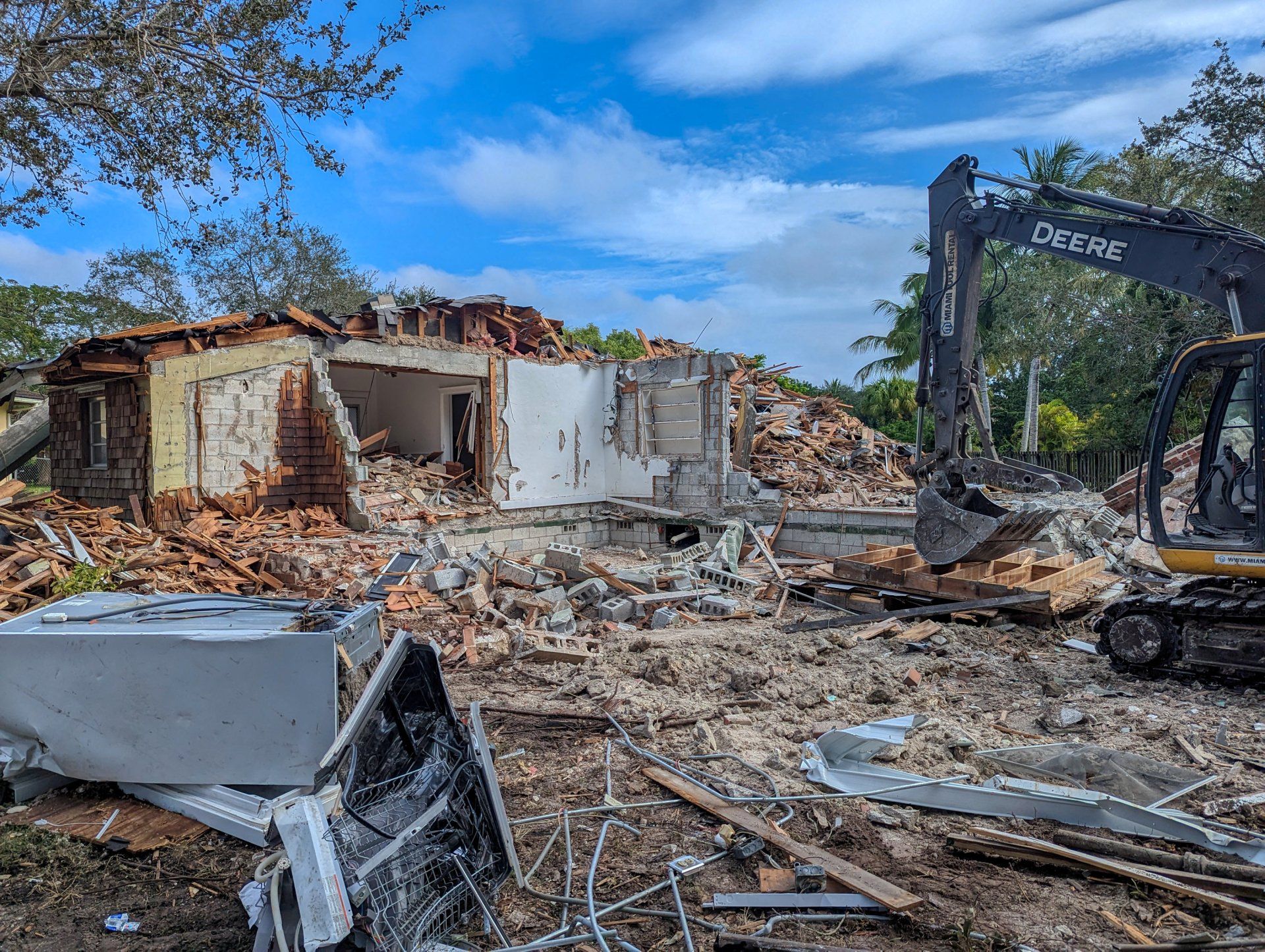Demolished brick building with a John Deere excavator under a cloudy sky.