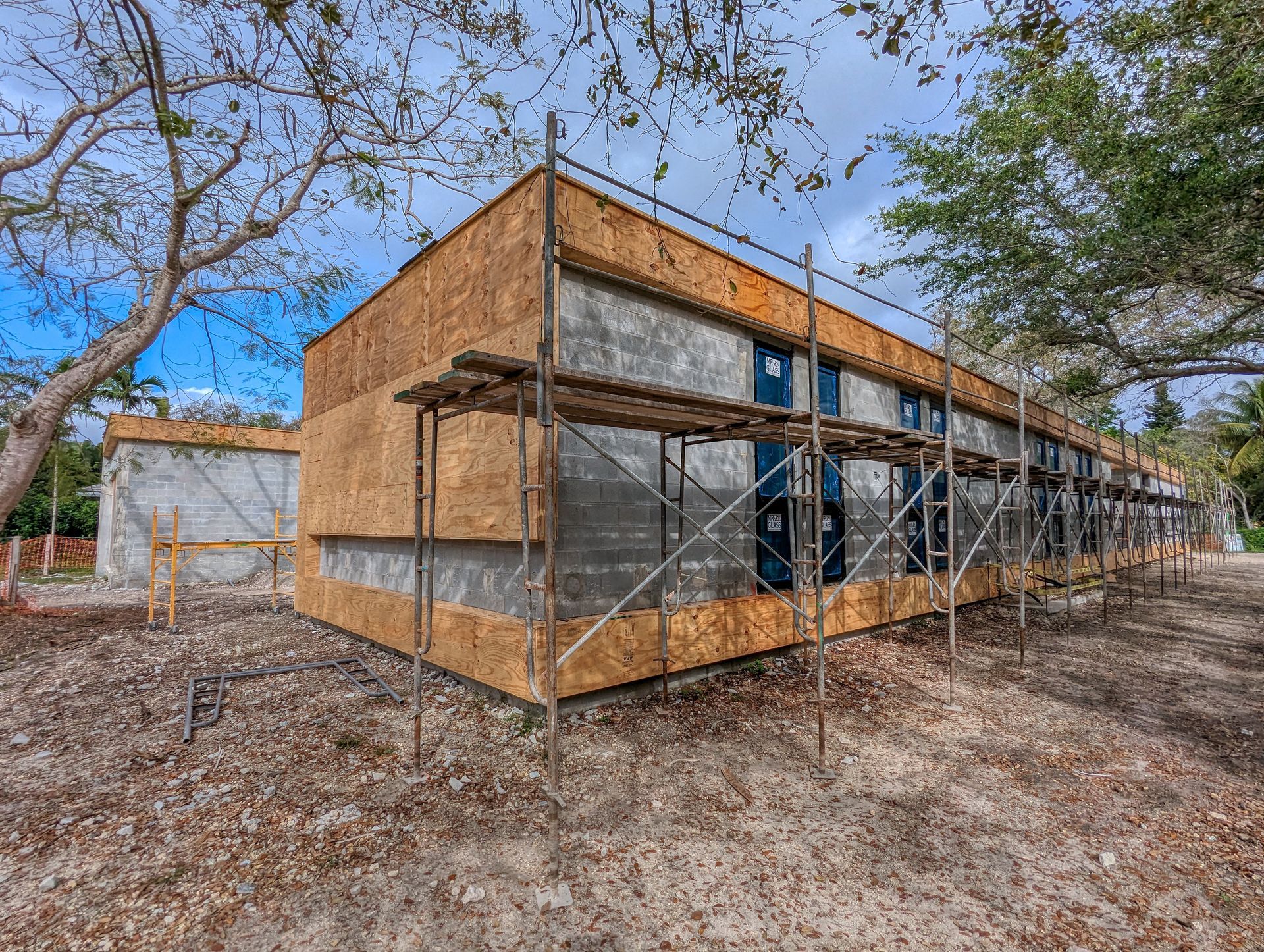 Building under construction with scaffolding; exterior walls covered in plywood and gray material.
