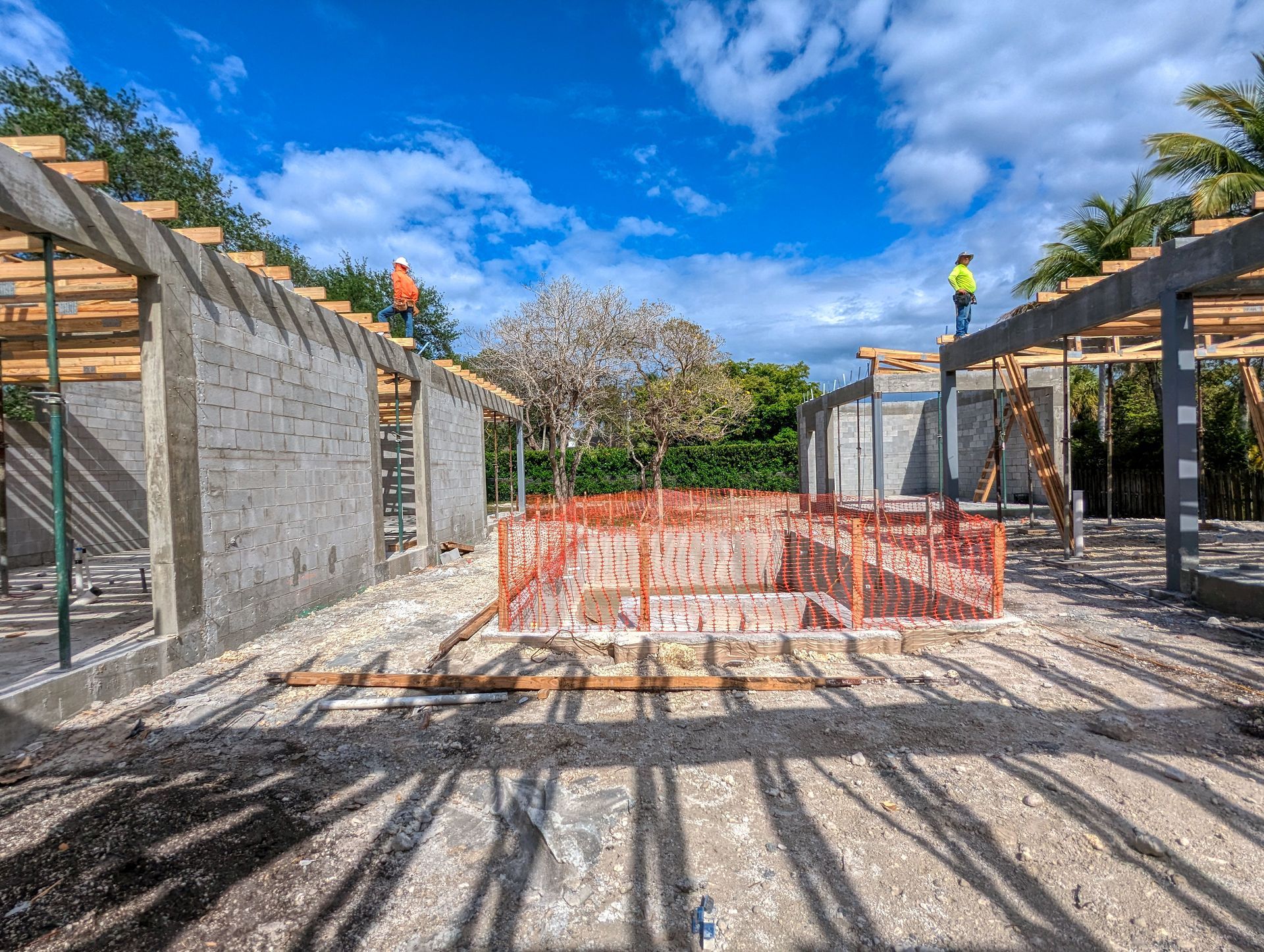 Construction site with concrete block walls, wooden framing, and workers under a blue sky.