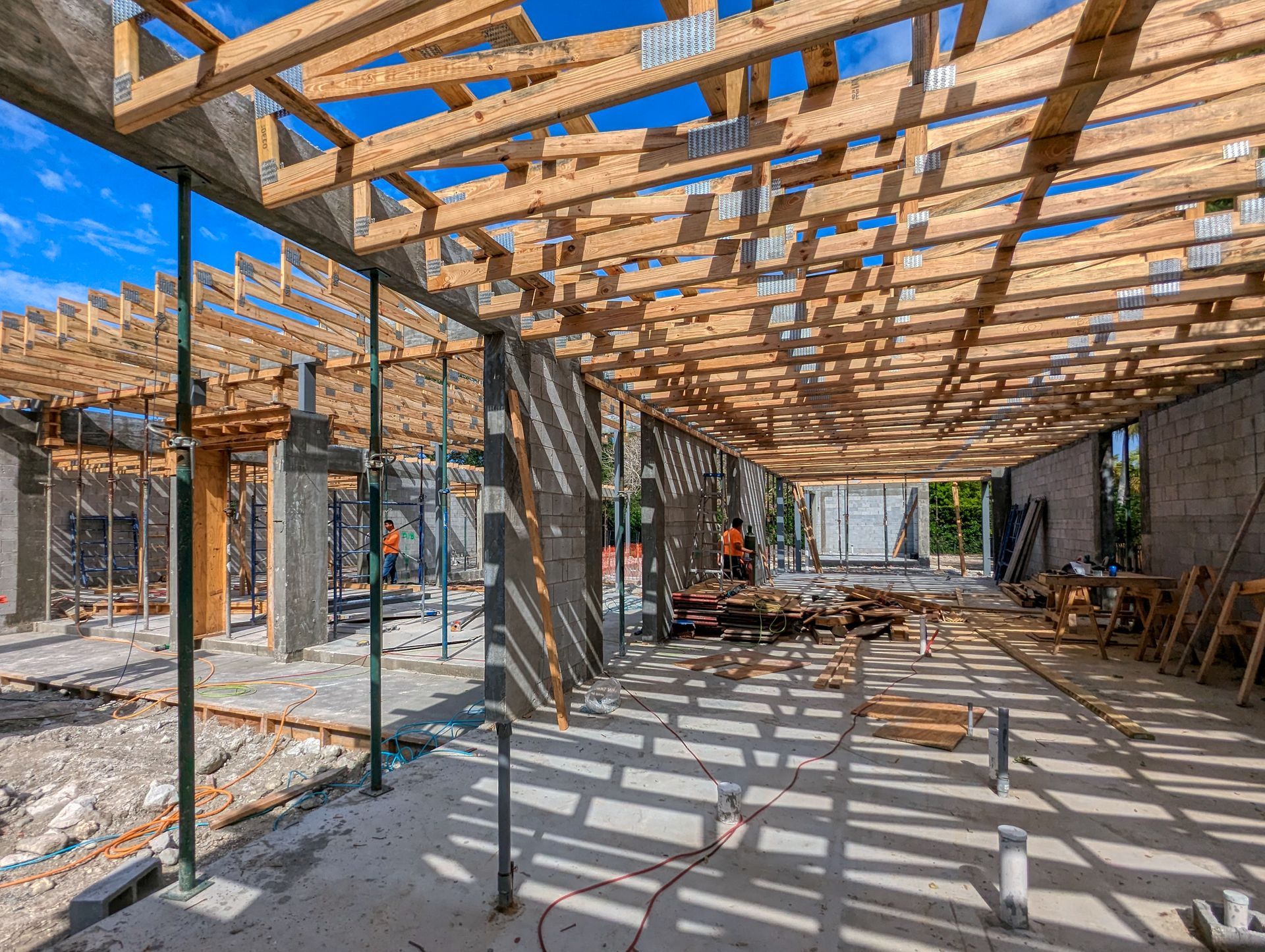 Construction site, building interior with exposed wooden rafters and concrete walls, bright sunlight.