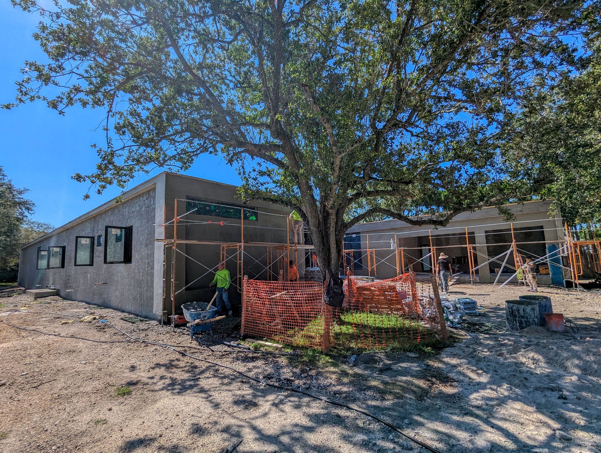 Building under construction with scaffolding, a tree, and a worker.