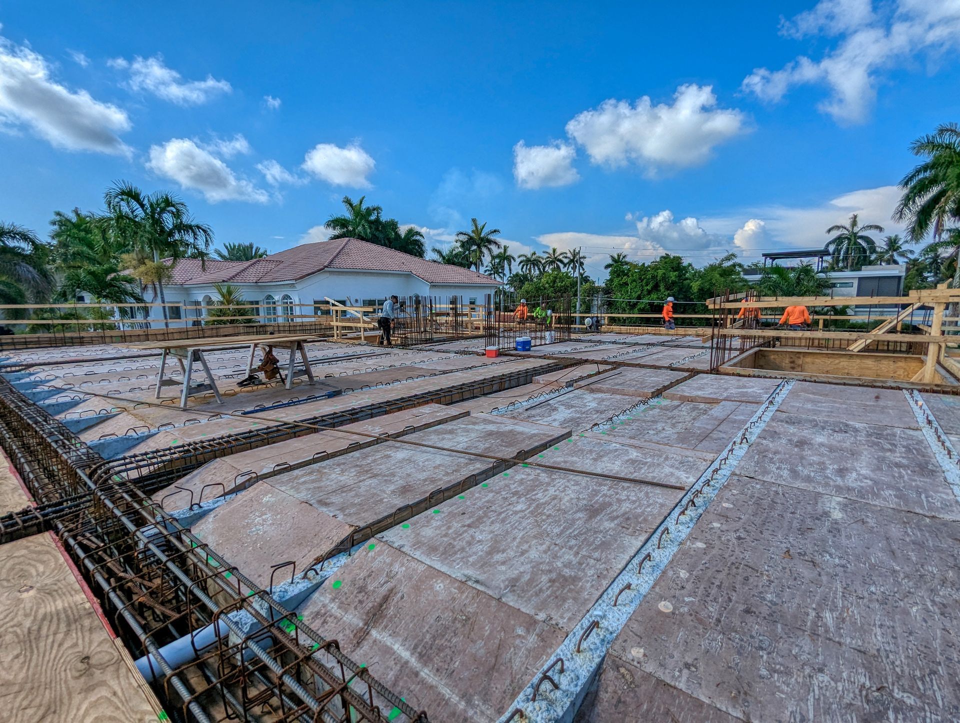 A construction site with a house in the background and a blue sky with clouds.