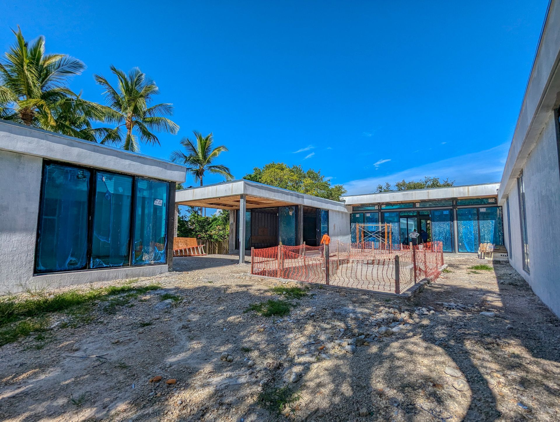 Exterior of a modern building under construction on a sunny day. Large windows covered in blue film.