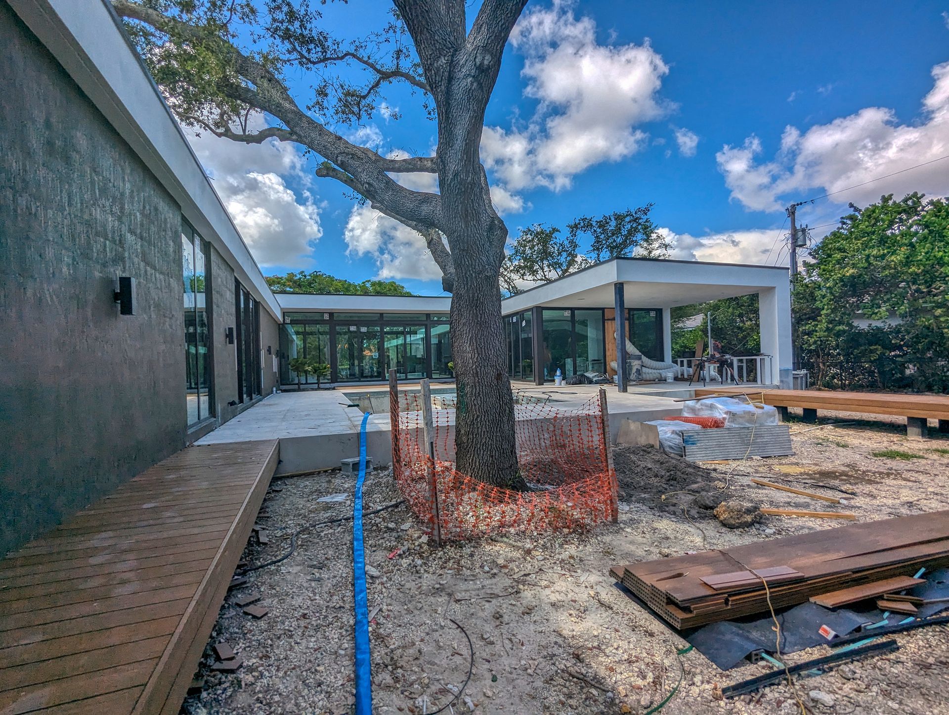A modern house under construction with a large tree in the center and a blue sky.