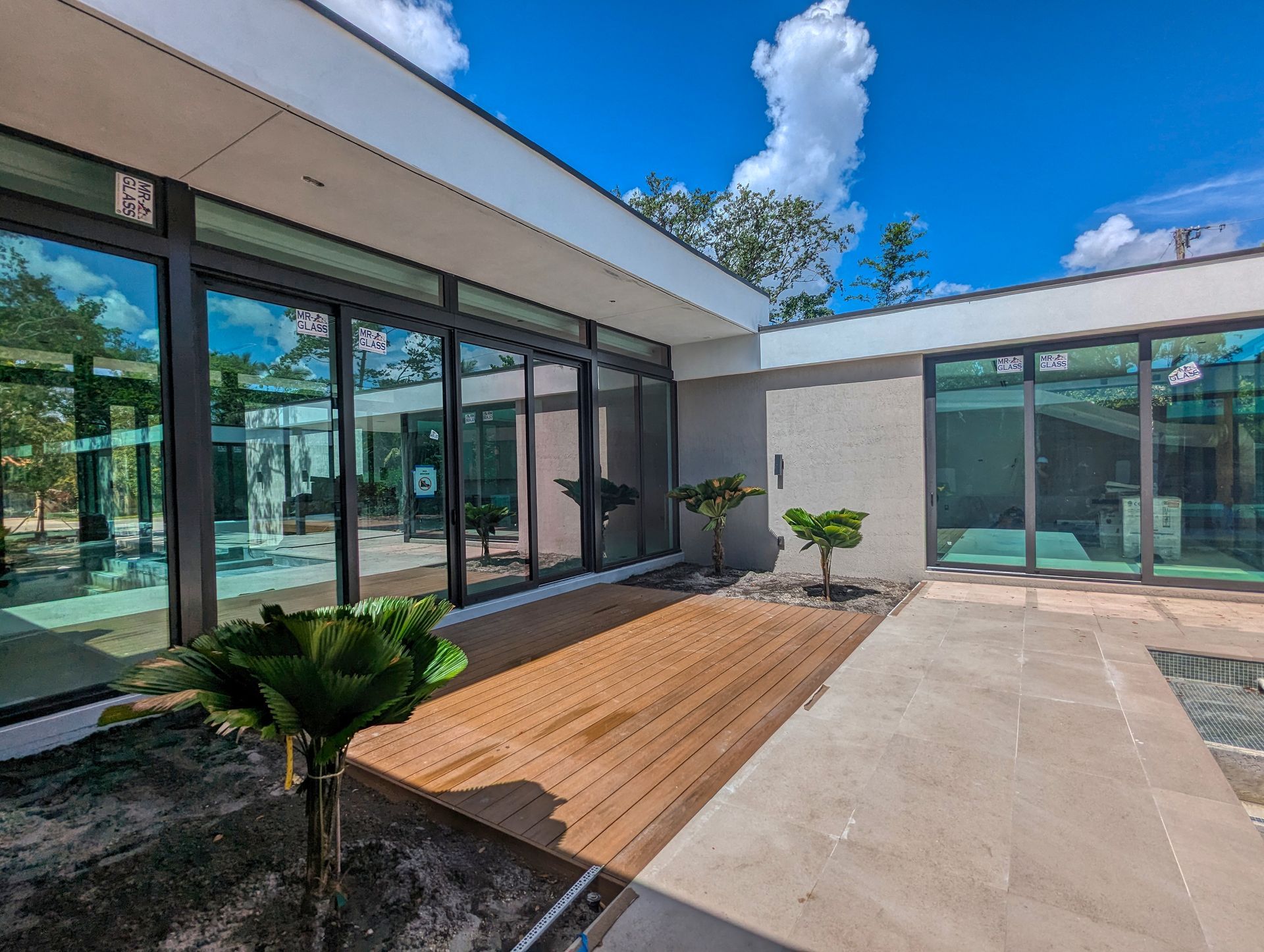 Modern building with floor-to-ceiling windows, wooden deck, small plants, and a bright blue sky.