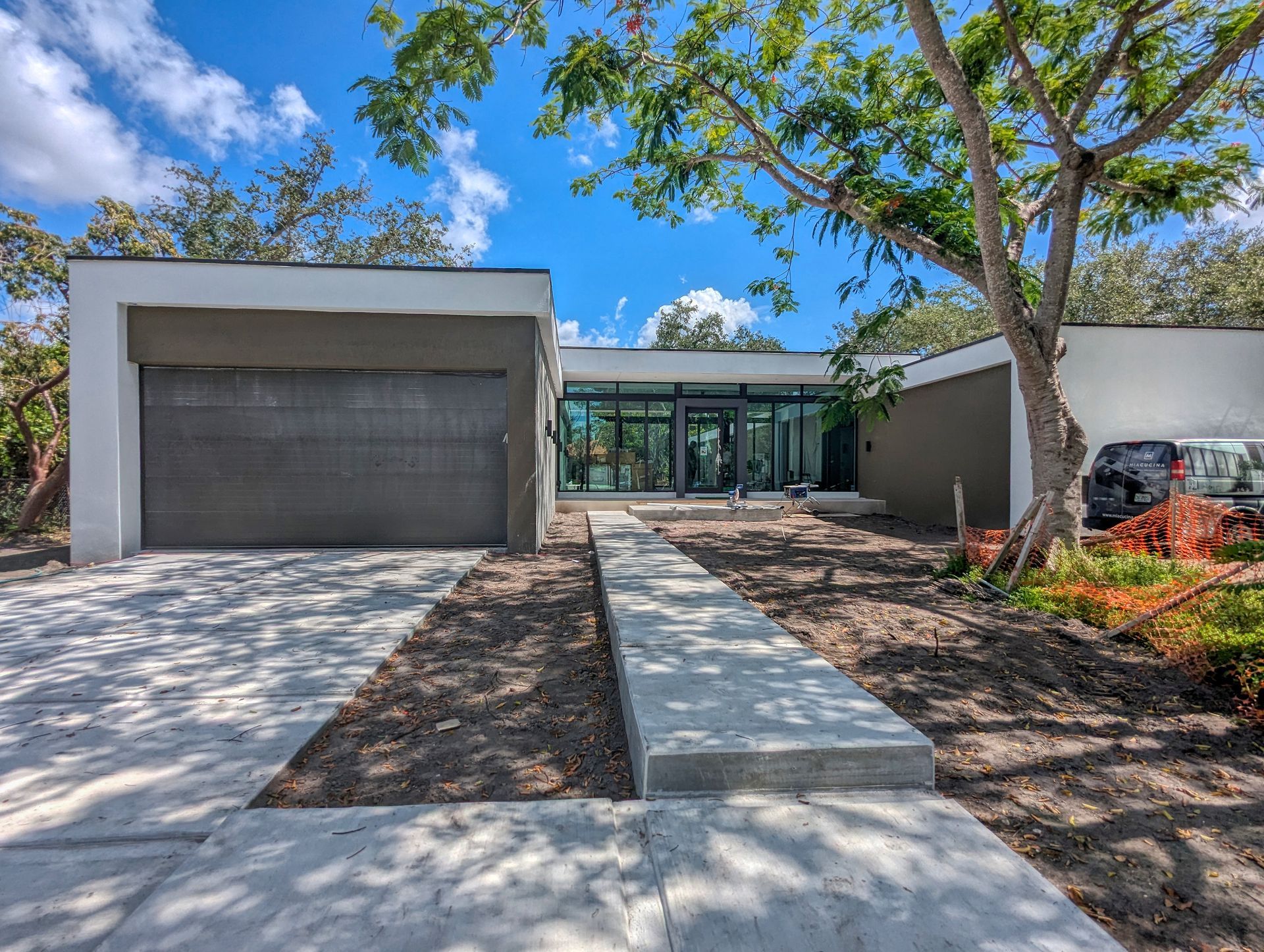 Modern house exterior with gray garage, glass front entrance, and concrete path under blue sky.