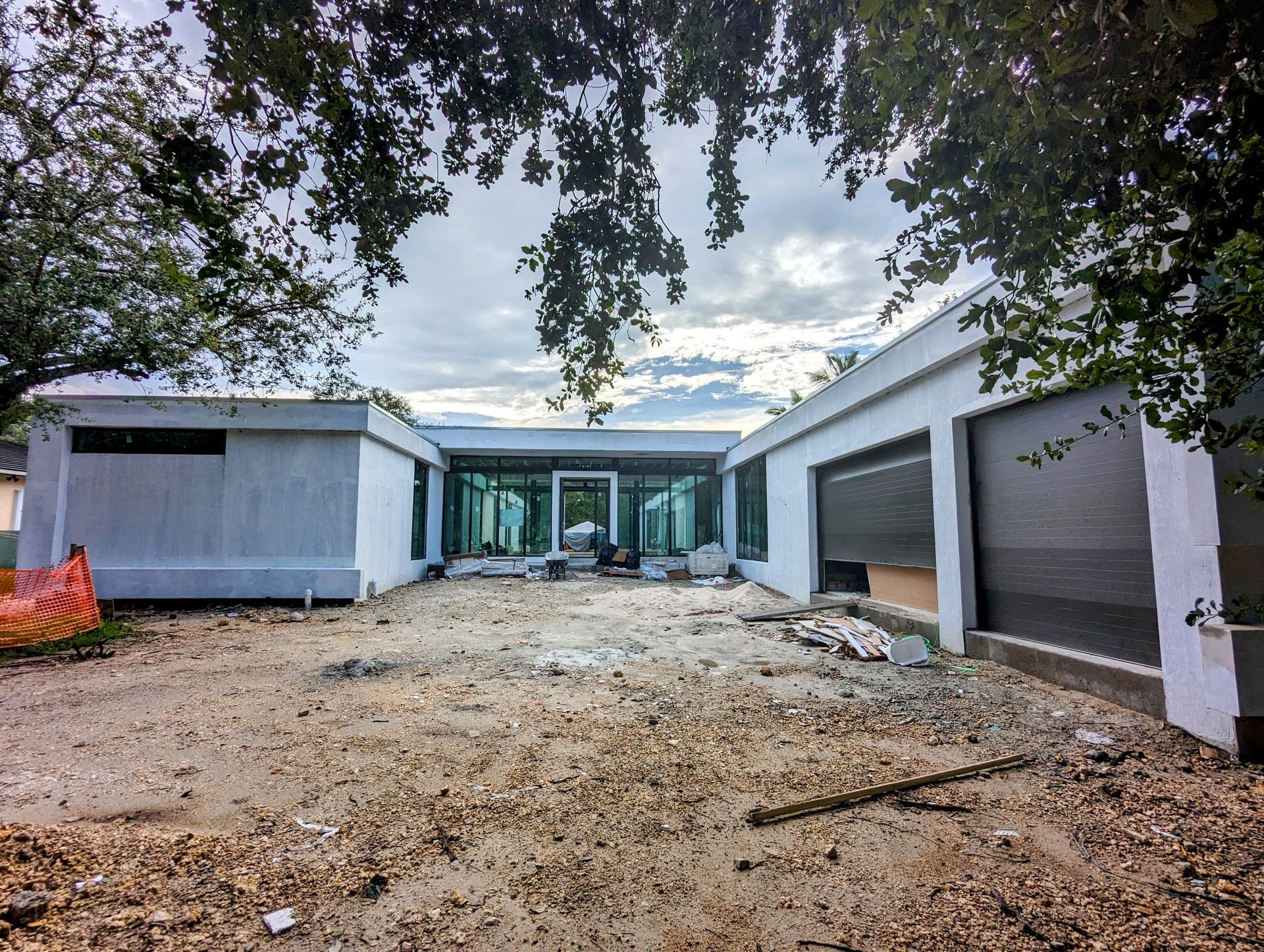 Exterior view of a modern house under construction. Light-colored walls, large windows, and a partially open garage door.