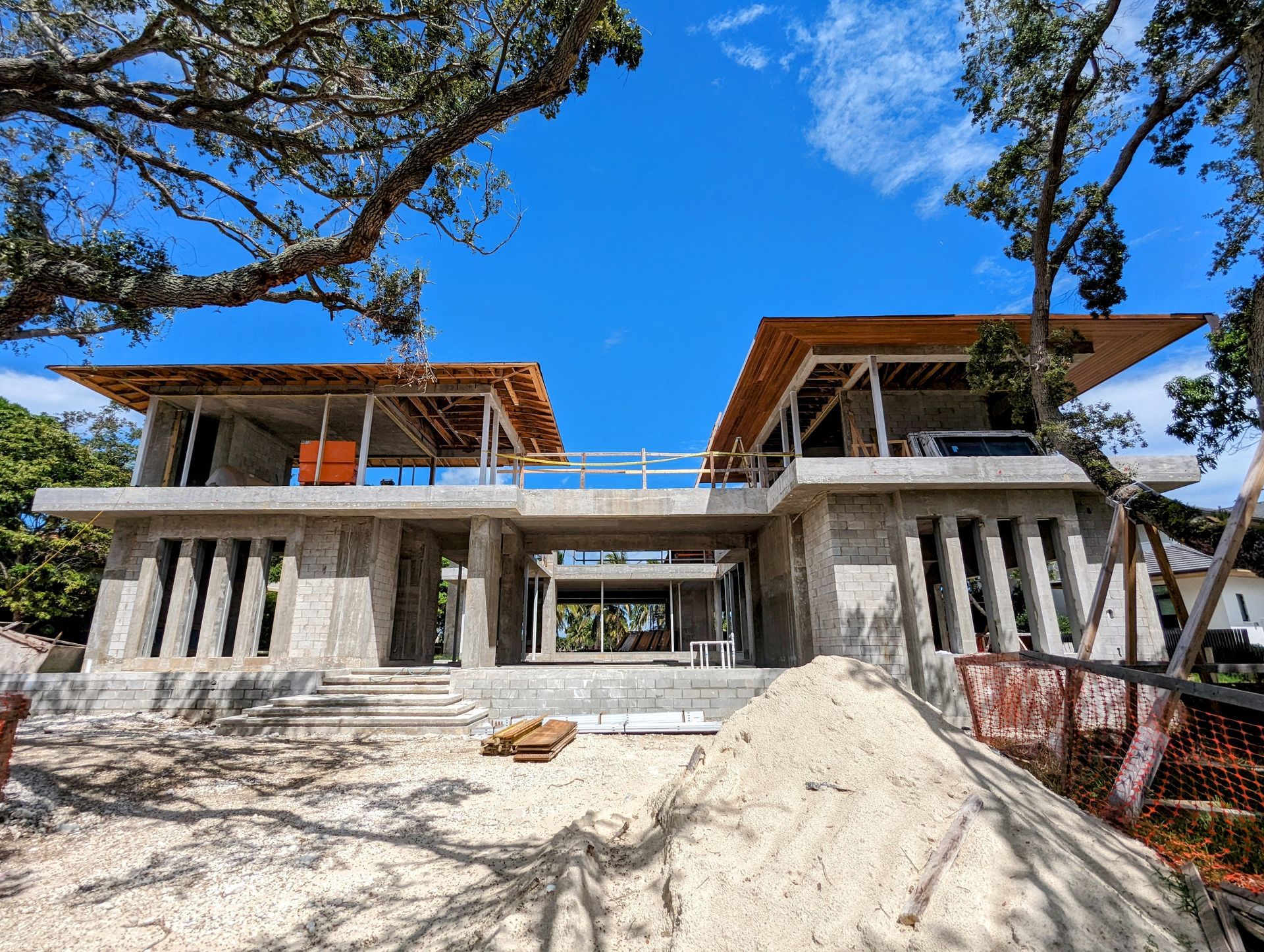 Construction of a two-story concrete building with a low-slung roof under a clear blue sky.