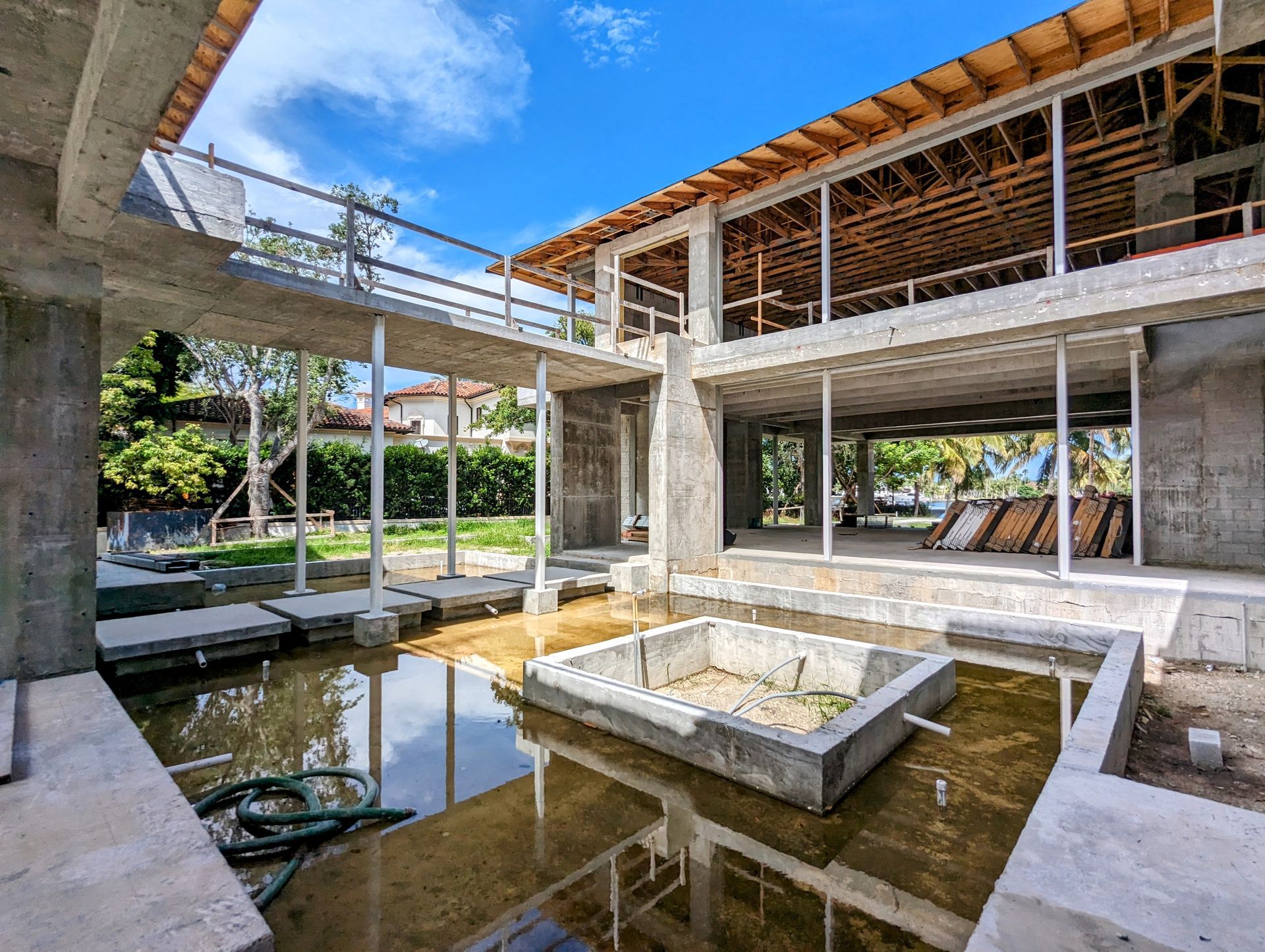 Construction site of a modern house, concrete structures, water feature, blue sky.