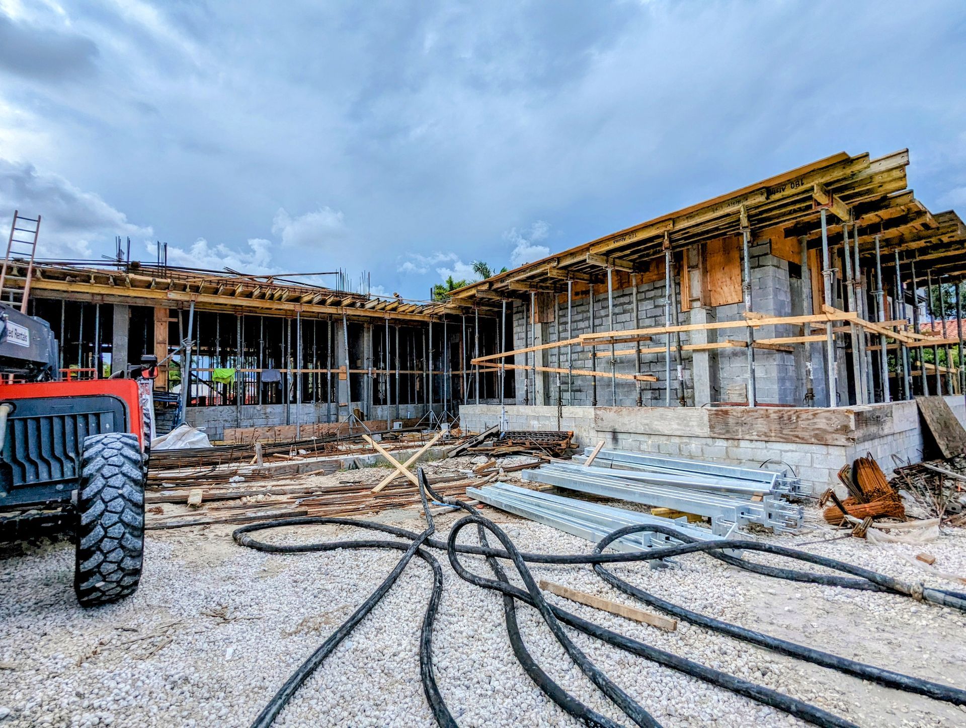 Construction site with wooden framing and concrete block walls under a cloudy sky.