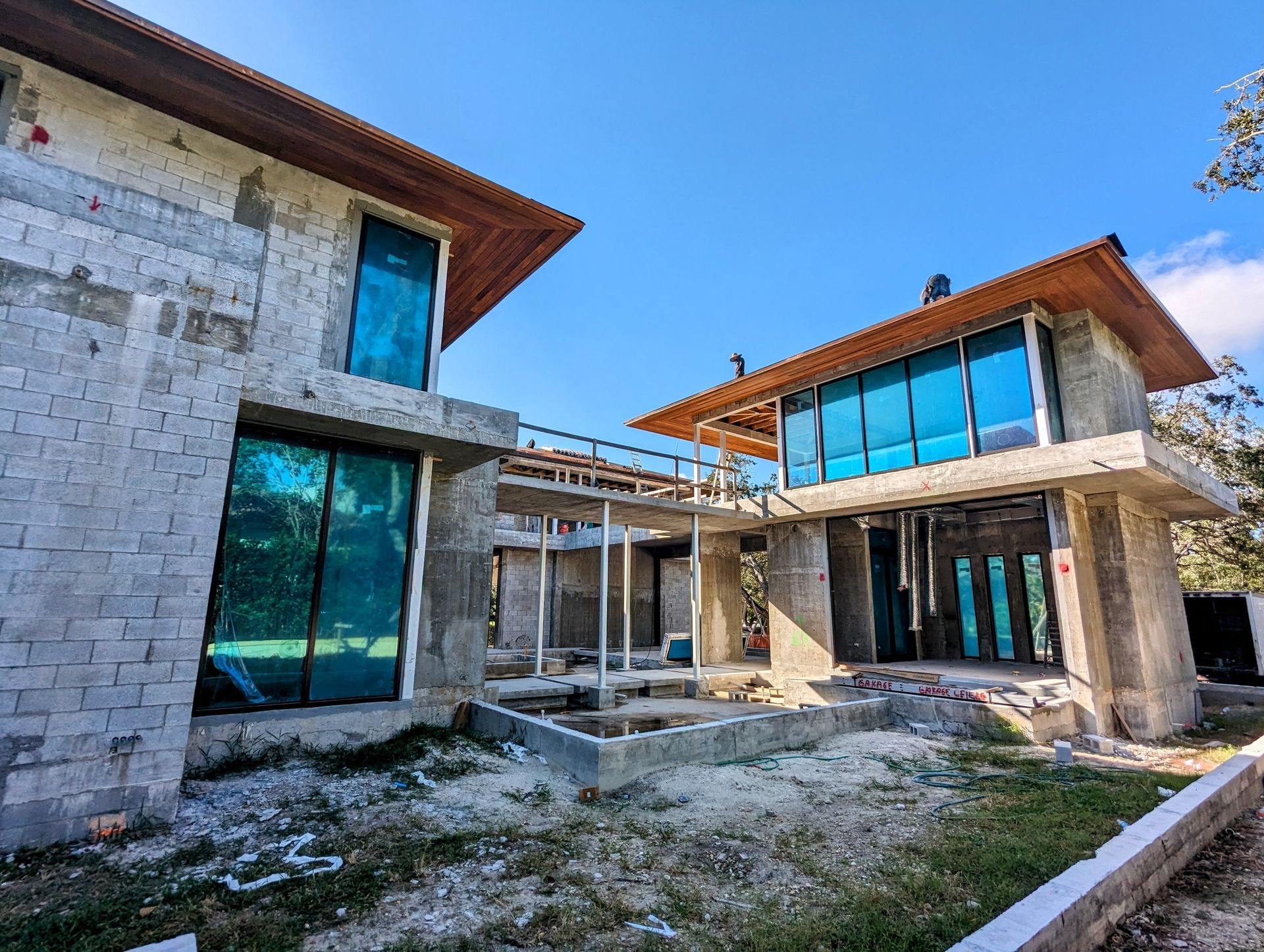Two unfinished concrete buildings with teal windows under a blue sky.
