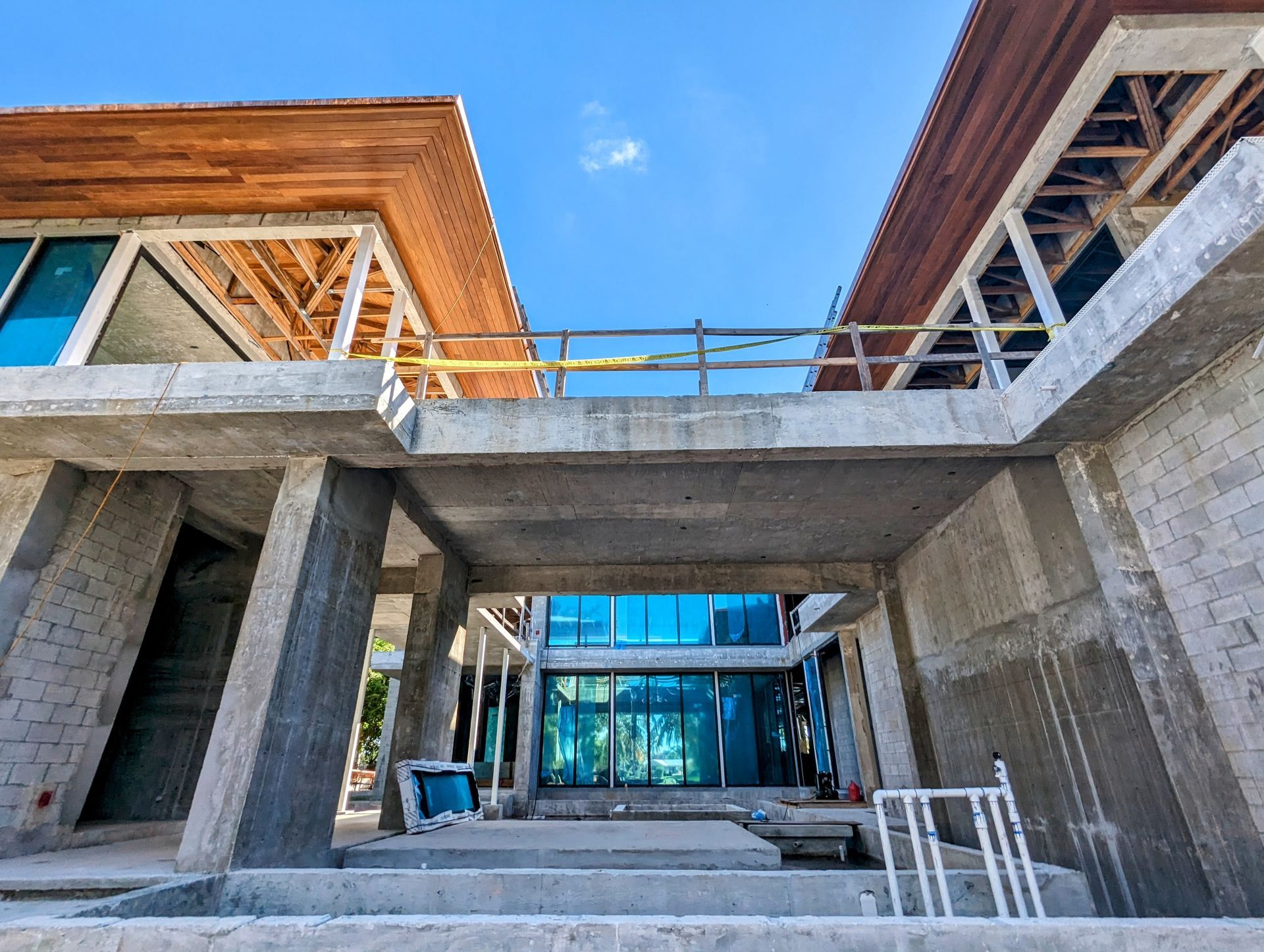 Concrete house under construction with glass windows, wooden roof, and safety railings.