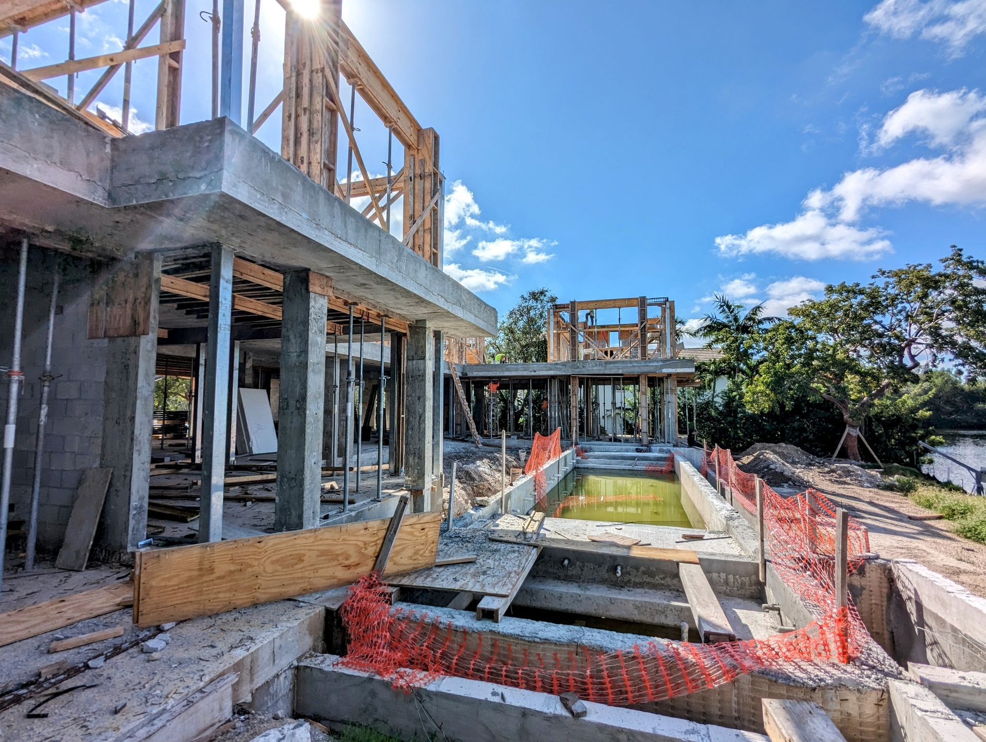 Construction site of a house with unfinished concrete walls and a swimming pool, bright sky.