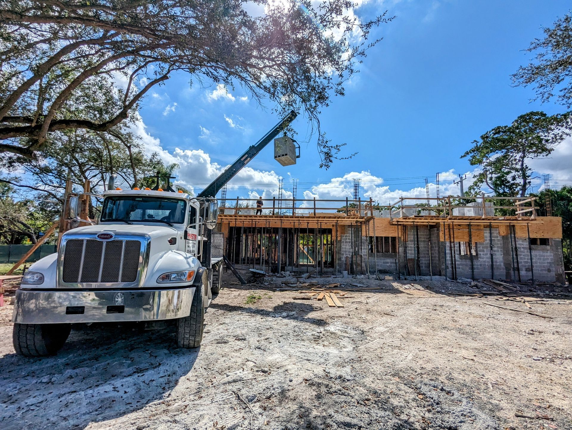 Construction site with a truck, crane, and partially built house under a bright blue sky.