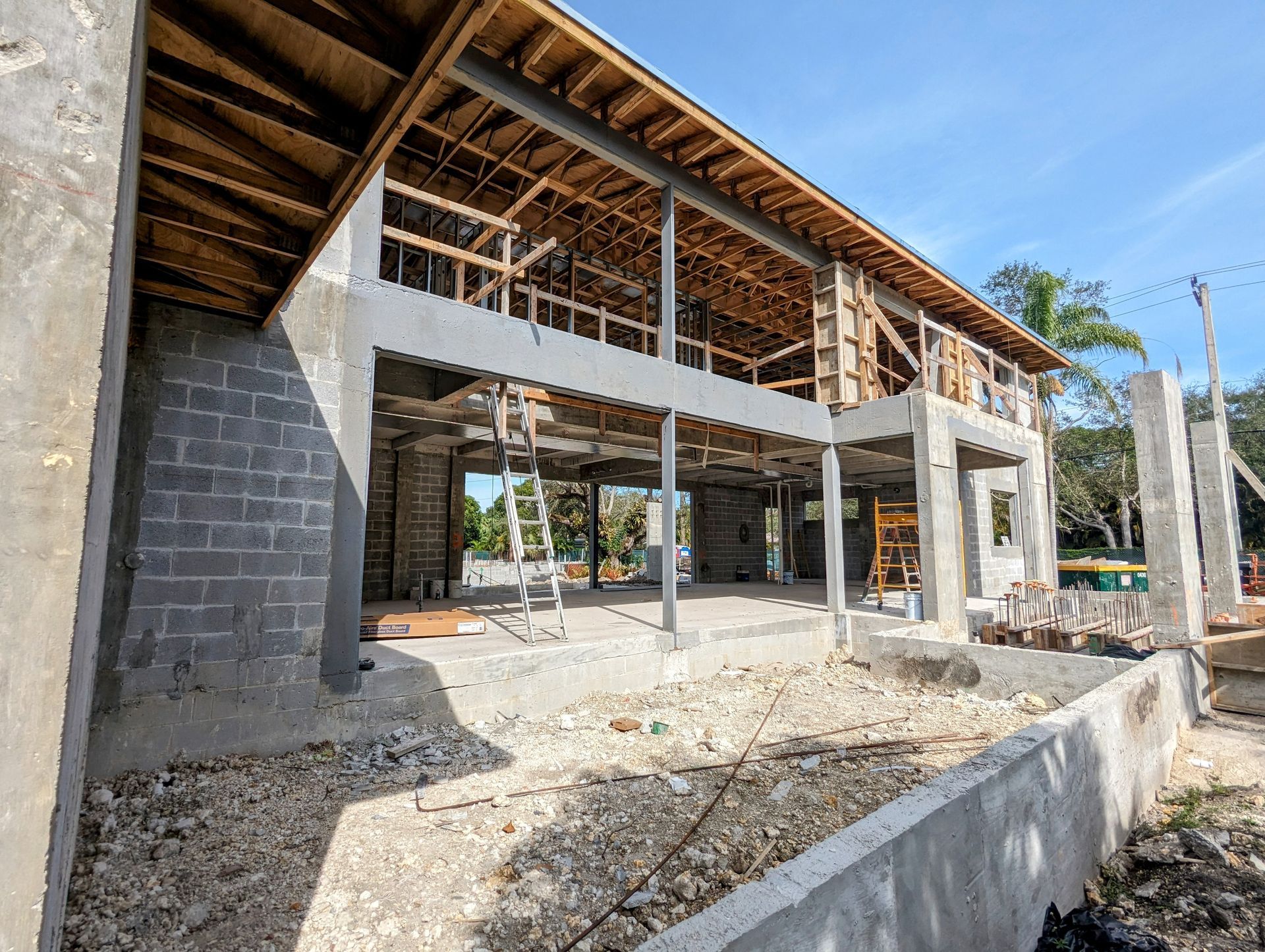 Construction of a two-story building; concrete and wood framing, unfinished walls, under blue sky.