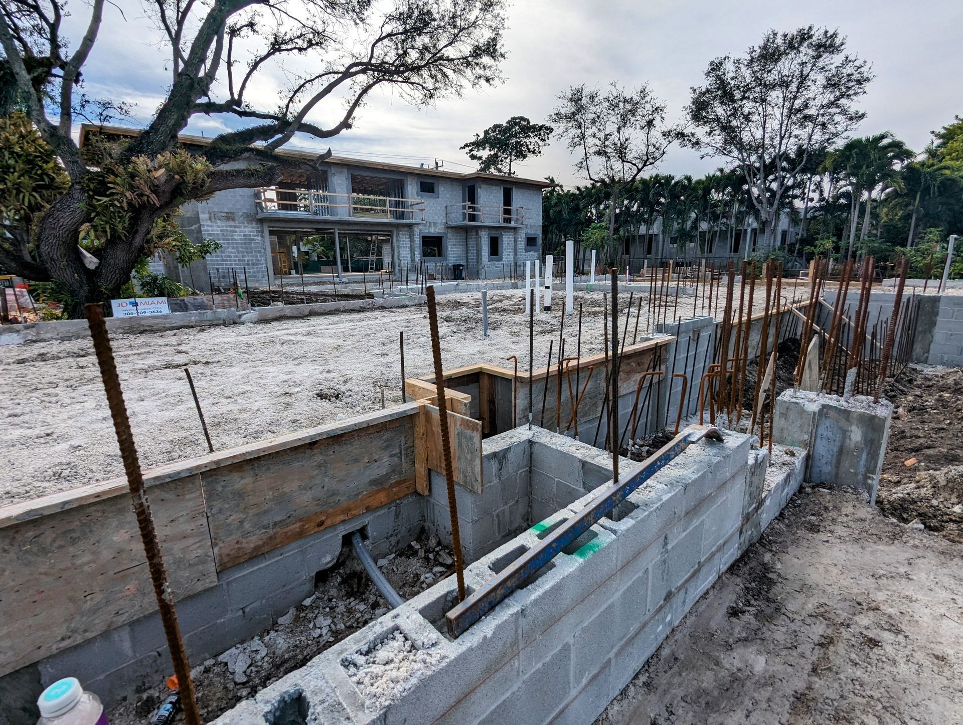 Construction site with concrete block walls, rebar, and partially built structure; overcast sky.