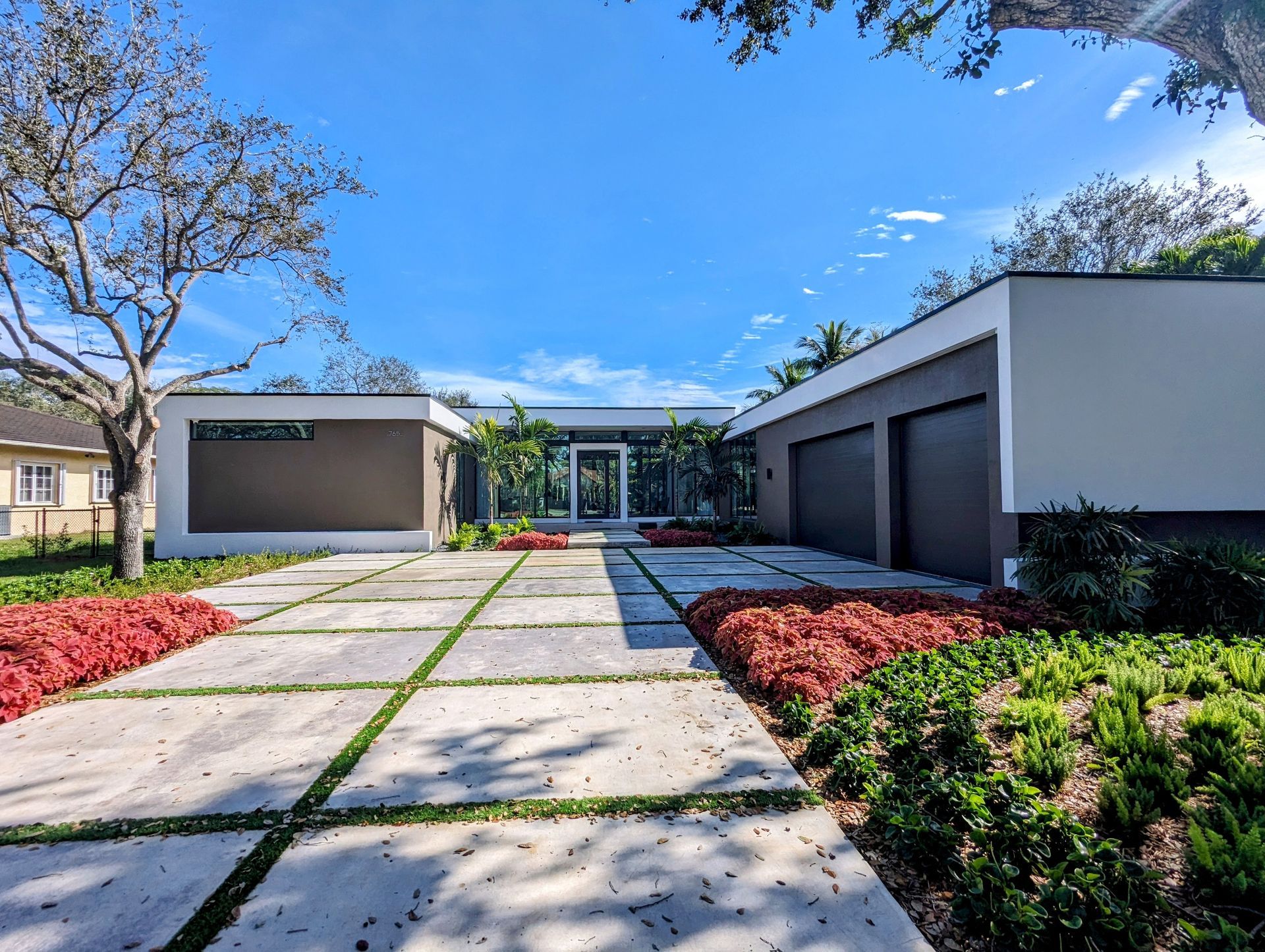 Modern home with concrete driveway, red flowers, and blue sky.
