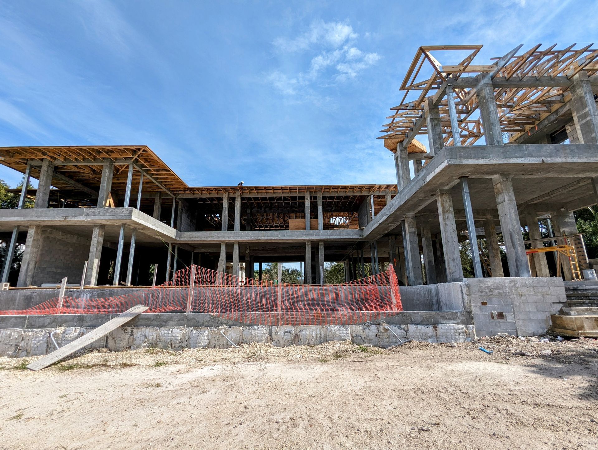 Construction site of a multi-story building, with exposed concrete framework and wooden beams, against a blue sky.