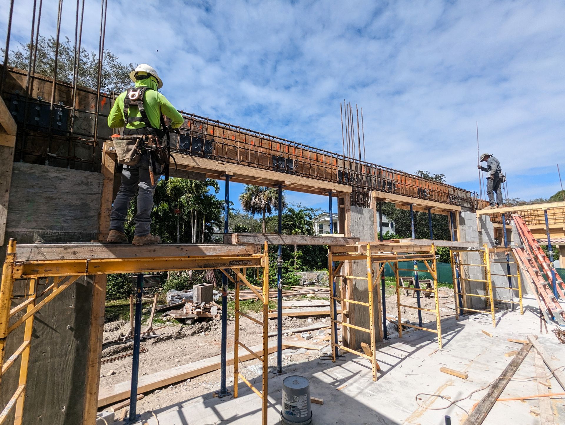 Construction workers on scaffolding, building concrete structure under blue sky.