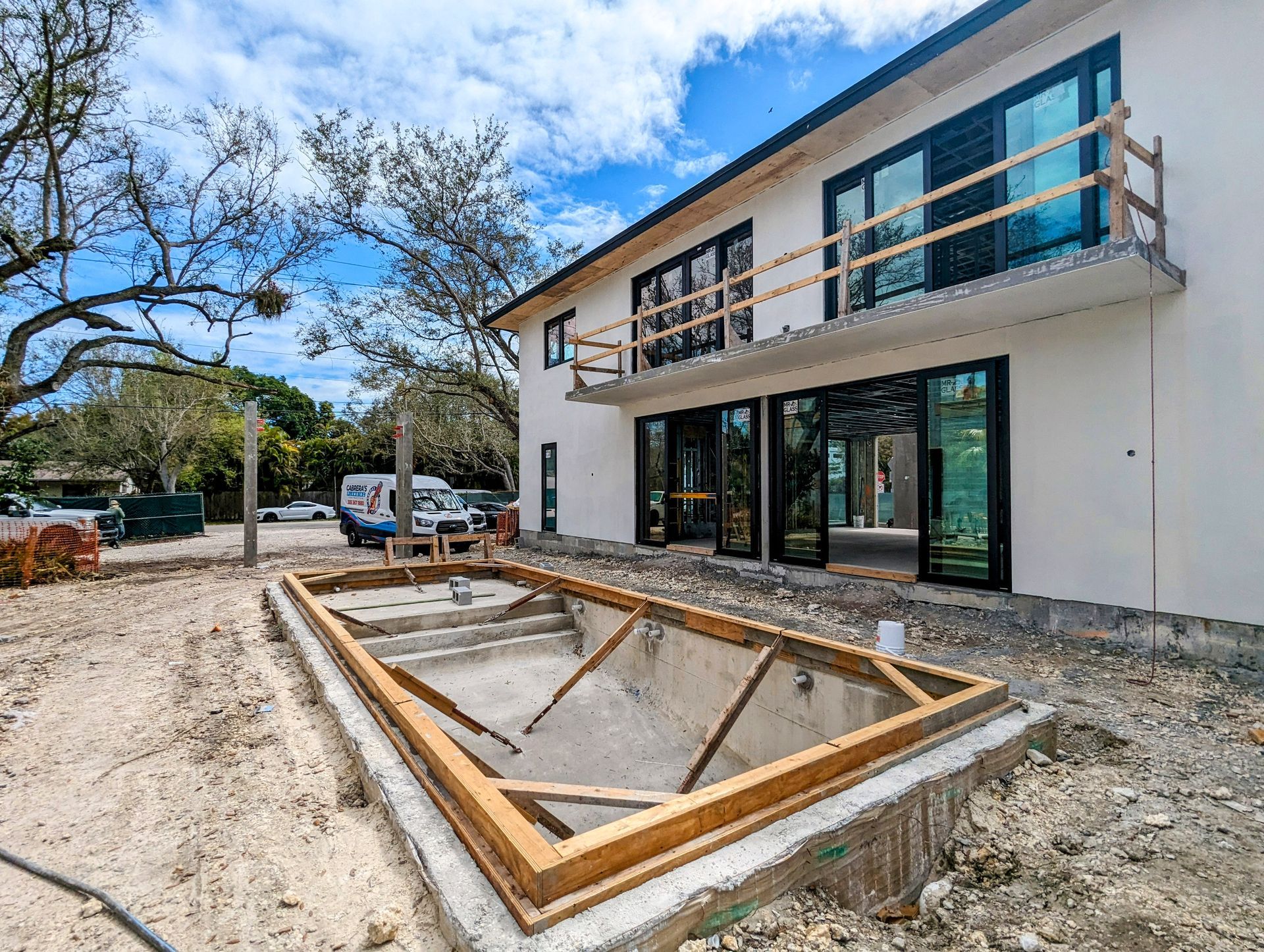 A two-story house under construction with a rectangular pool, on a sunny day.