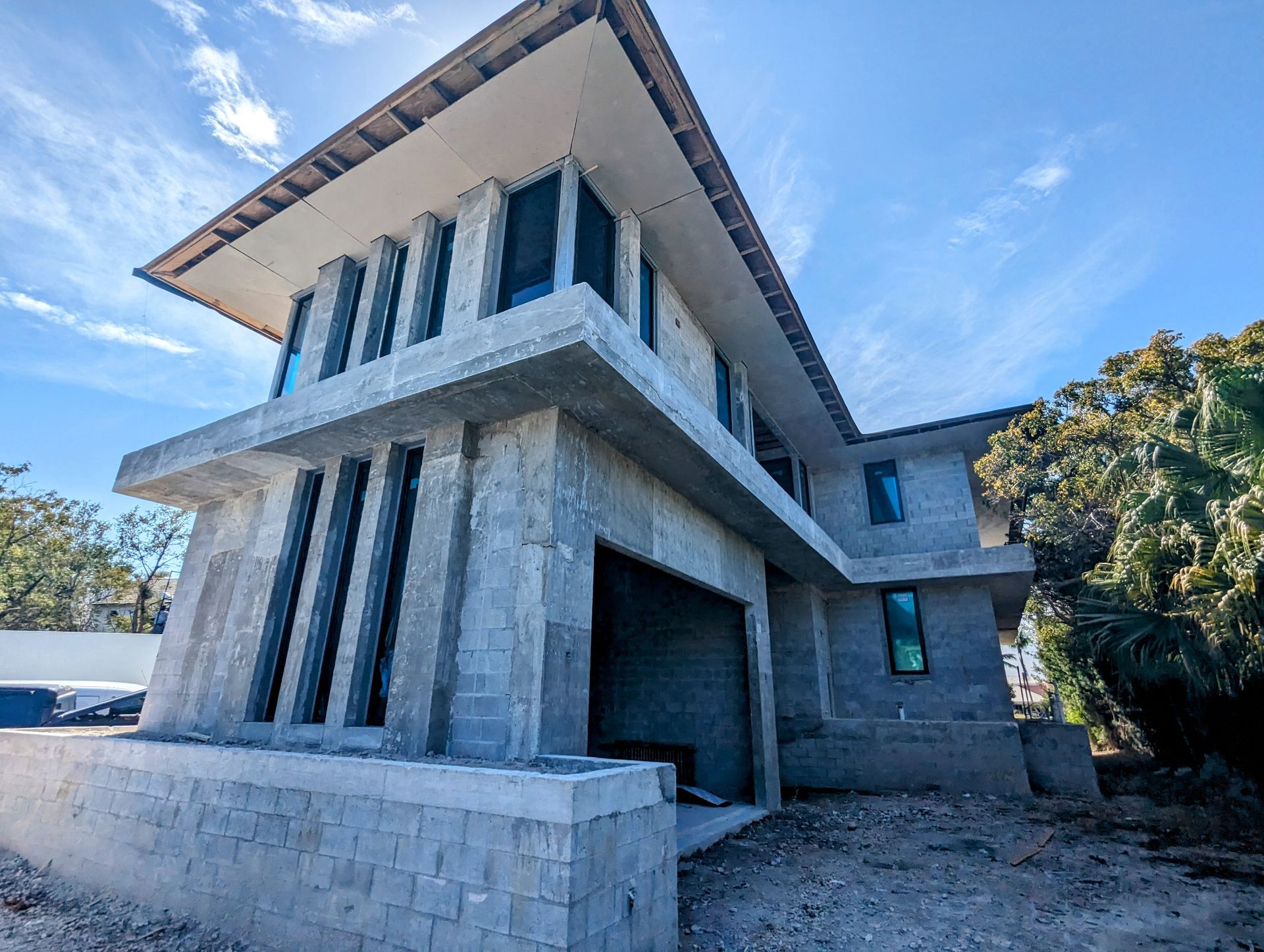 Two-story, unfinished concrete house with black-framed windows and a flat roof, under a blue sky.