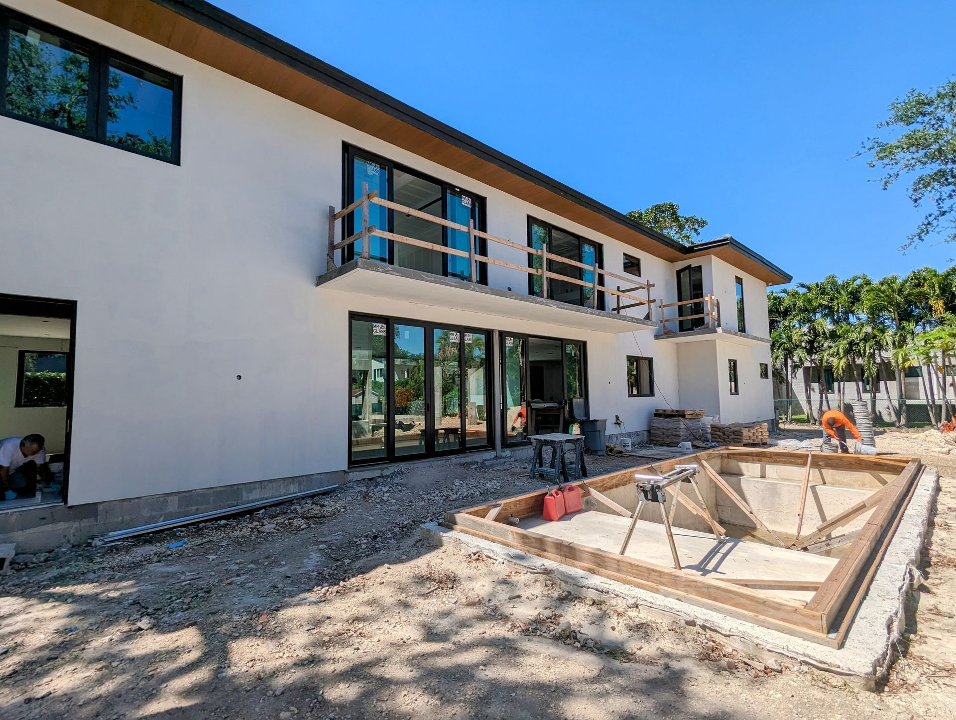 Exterior of a house under construction with a rectangular pool framework and workers.