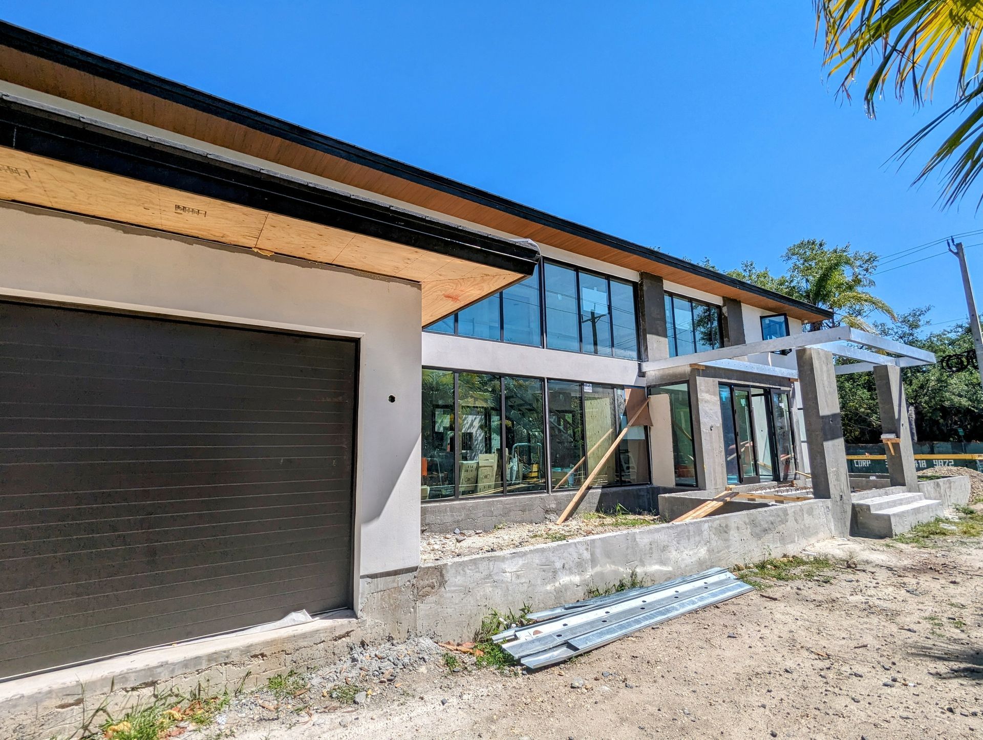 Modern two-story house under construction with large windows and a garage door; clear blue sky.