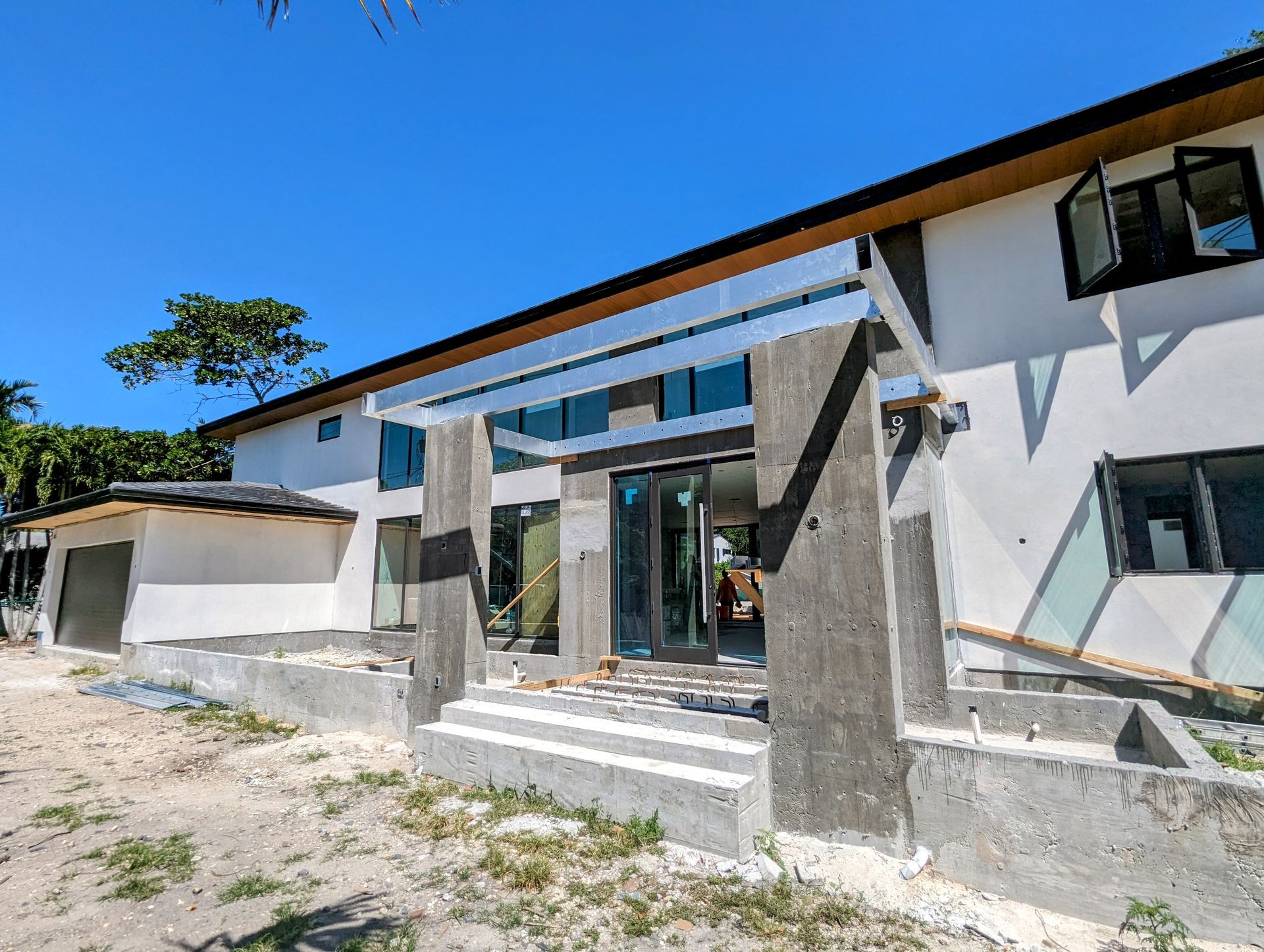 Two-story building under construction with concrete pillars, steps, and a glass door.