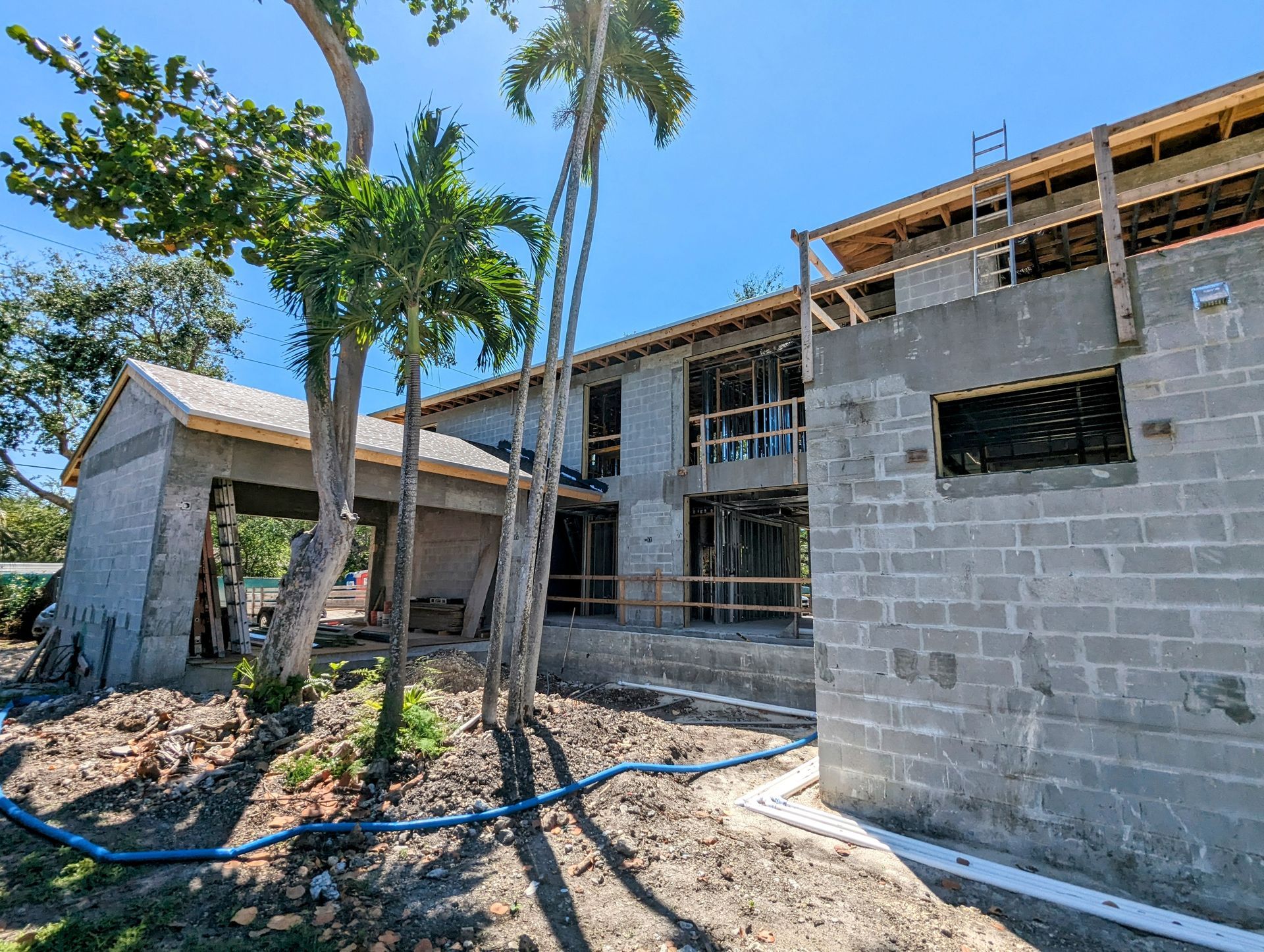 A two-story building under construction with exposed concrete block walls and wooden framing, outdoors on a sunny day.