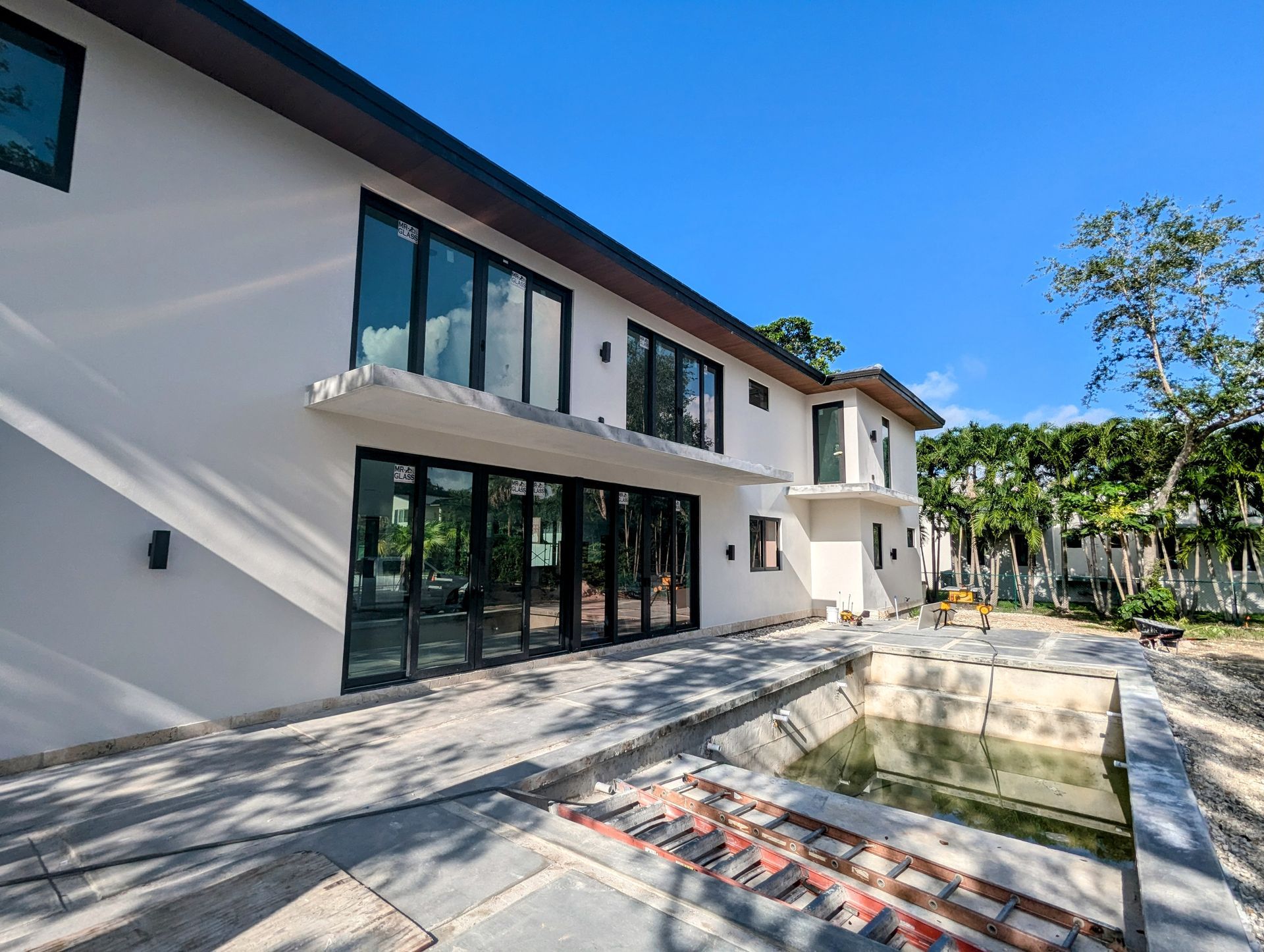 Modern white house with dark framed windows and a partially constructed pool, blue sky.