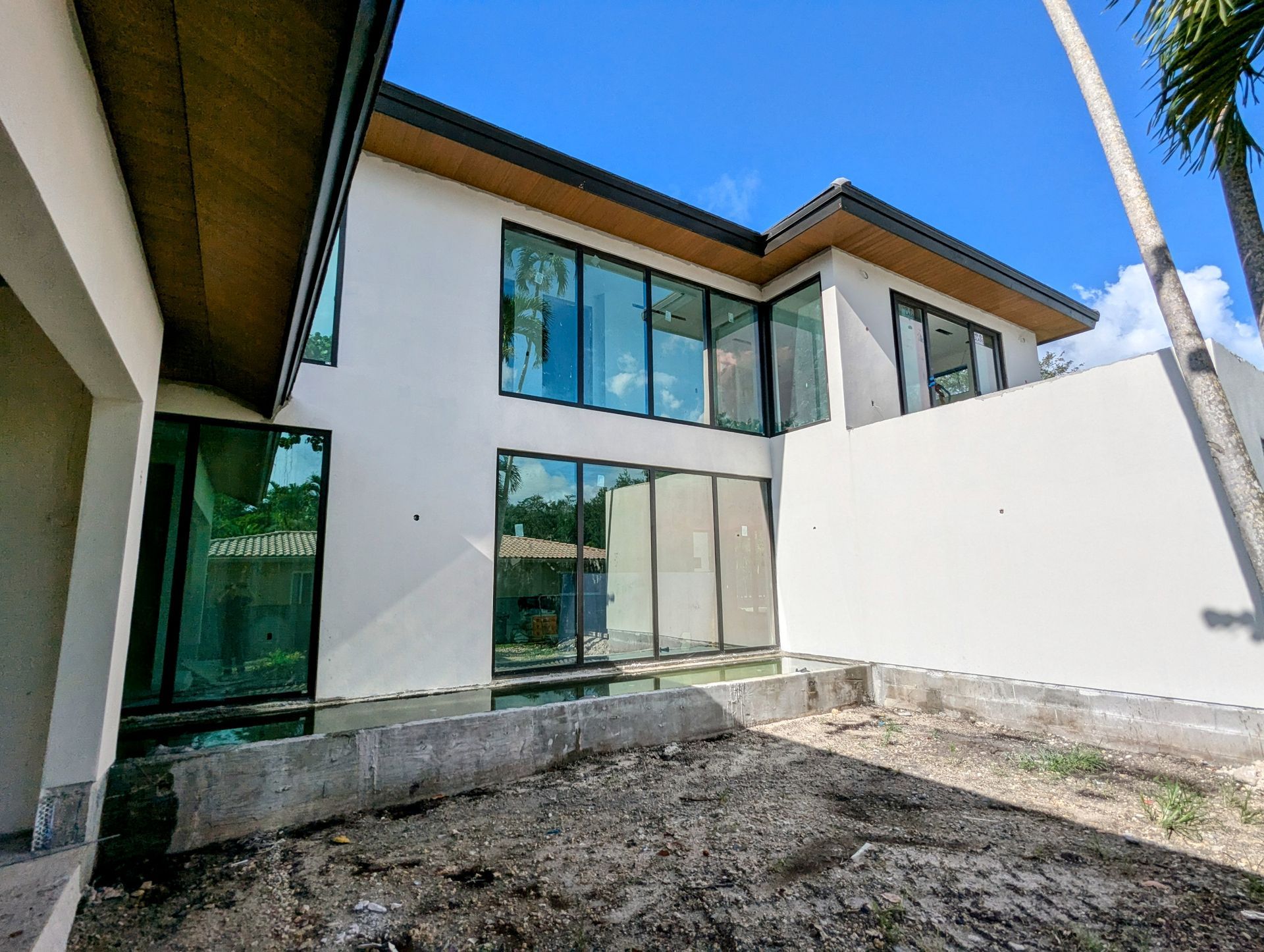 Modern white house with large windows, set on a construction site with dirt and a clear sky.