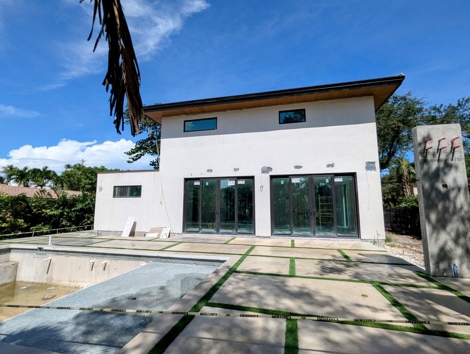 Modern two-story house under construction with sliding glass doors, unfinished pool, and concrete patio.